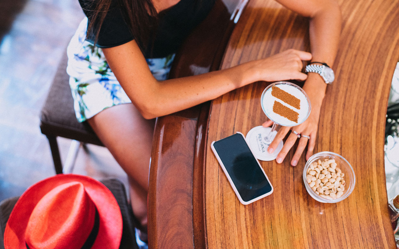 Chica sentada en el bar del hotel, tomando un cóctel con un logotipo de canela del Pestana Hotel Group