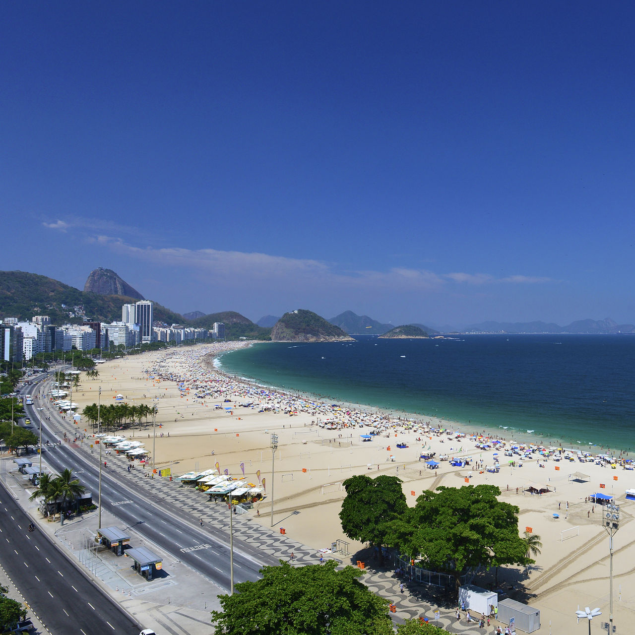 Playa de Copacabana en Río de Janeiro, playa concurrida con arena dorada, mar azul y montañas al fondo