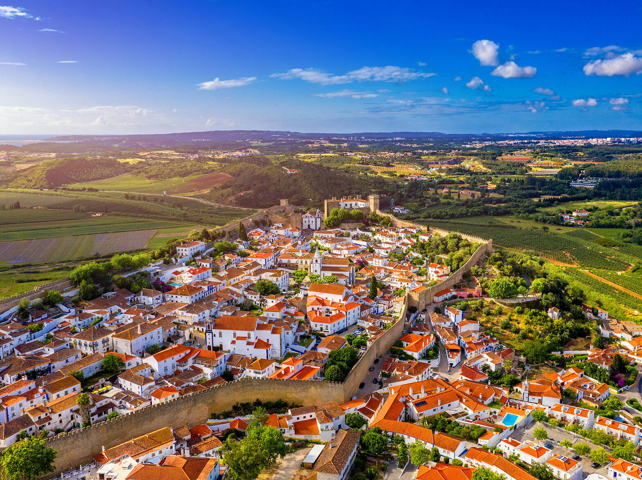 Vista aérea de un pueblo rodeado de campos verdes, con parte del pueblo rodeado de murallas