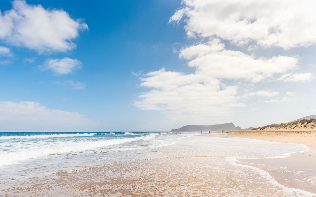 Playa extensa en Porto Santo con arena clara, olas calmadas y un cielo azul con algunas nubes