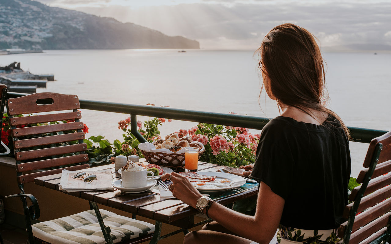 Senhora toma o pequeno-almoço na esplanada de restaurante com vista para o oceano, num hotel com vista para o mar