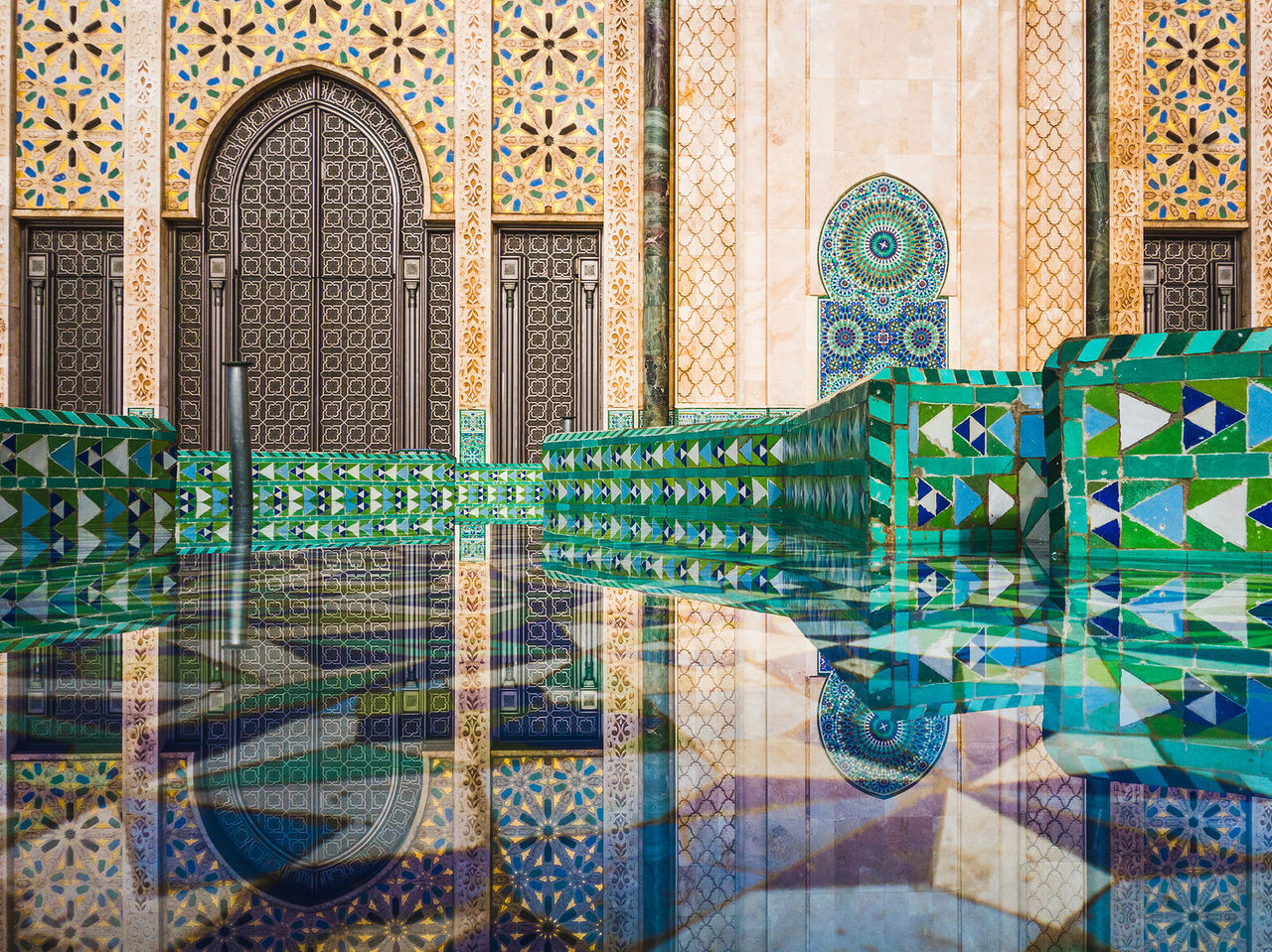 O reflexo do interior de uma mesquita, cheio de cores vibrantes e com padrões simétricos tipicamente marroquinos