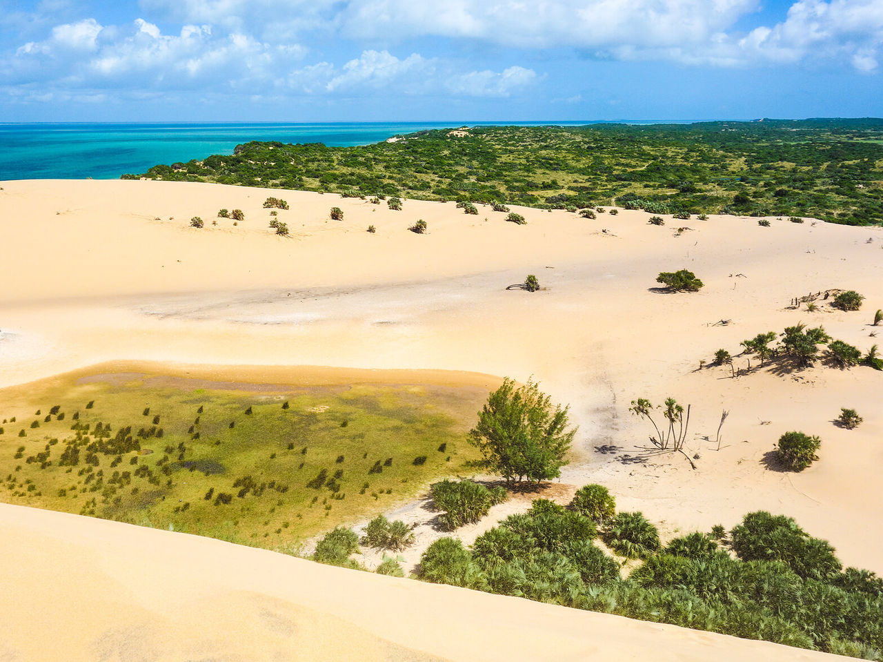 Vista aérea de uma paisagem desértica com dunas de areia branca em contraste com as águas cristalinas do oceano