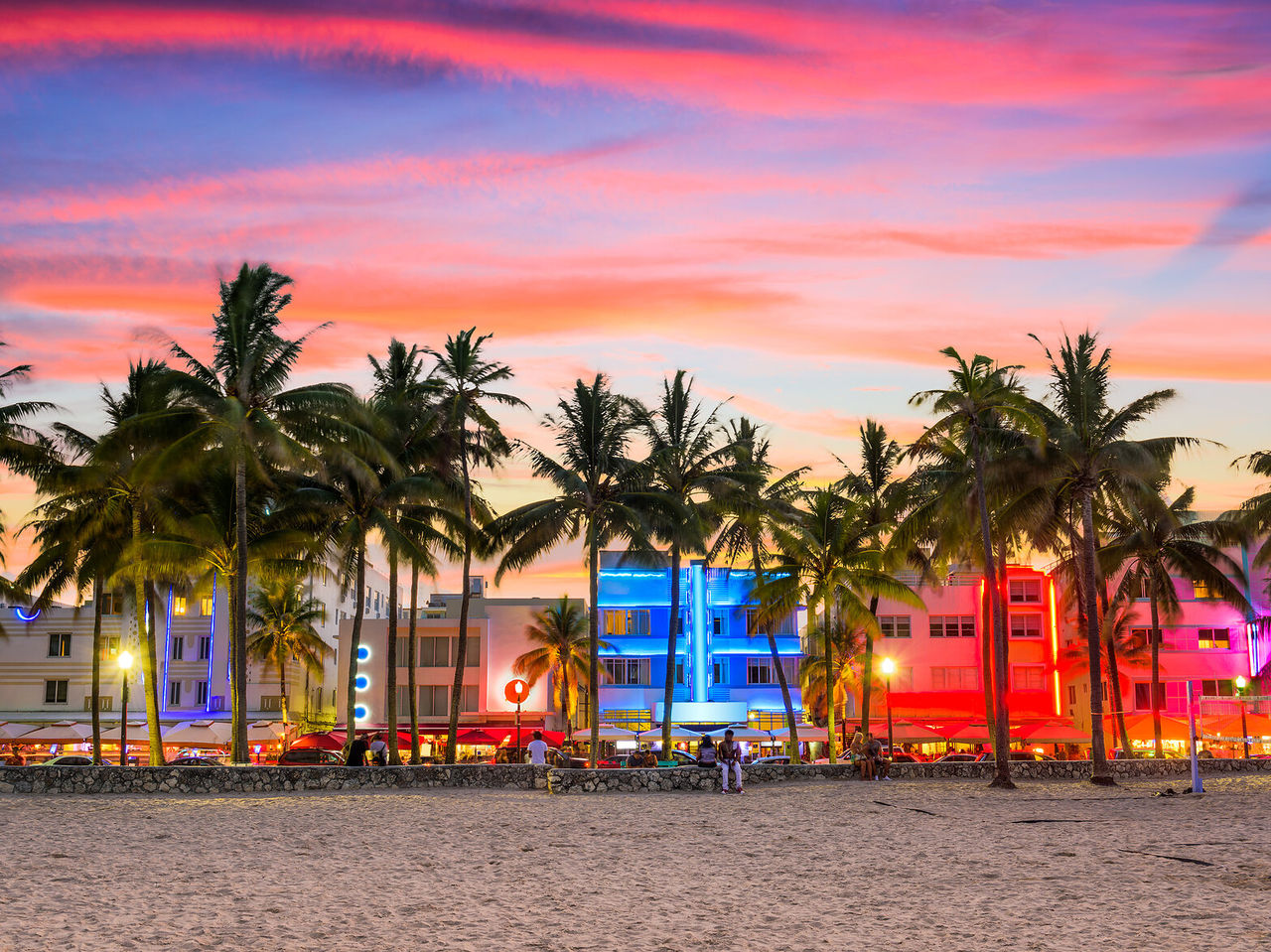 Pôr do sol vibrante em Miami Beach, com palmeiras silhuetas e edifícios arte déco iluminados 