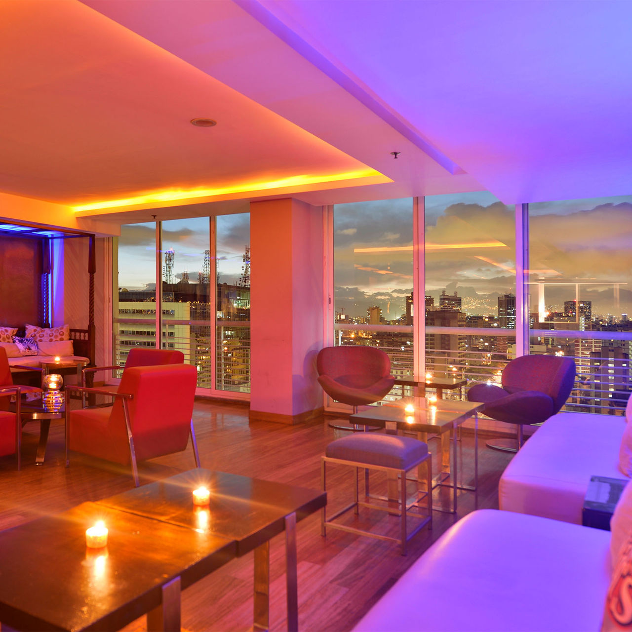Bar do Pestana Caracas com vista panorâmica da cidade ao entardecer, um espaço moderno com sofás e poltronas