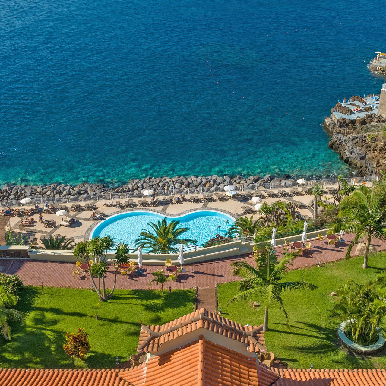 Vista aérea do Pestana Vila Lido Madeira, com vista para o mar, palmeiras à volta e uma piscina