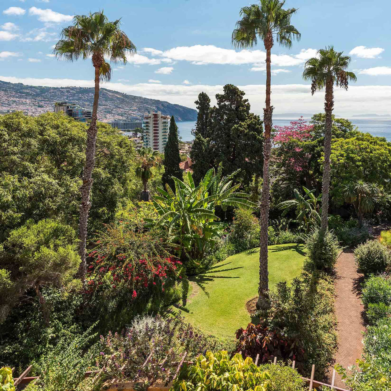 Jardim com várias plantas tropicais, vista para o mar e colina do Pestana Village, um Hotel Romântico no Funchal, na Madeira