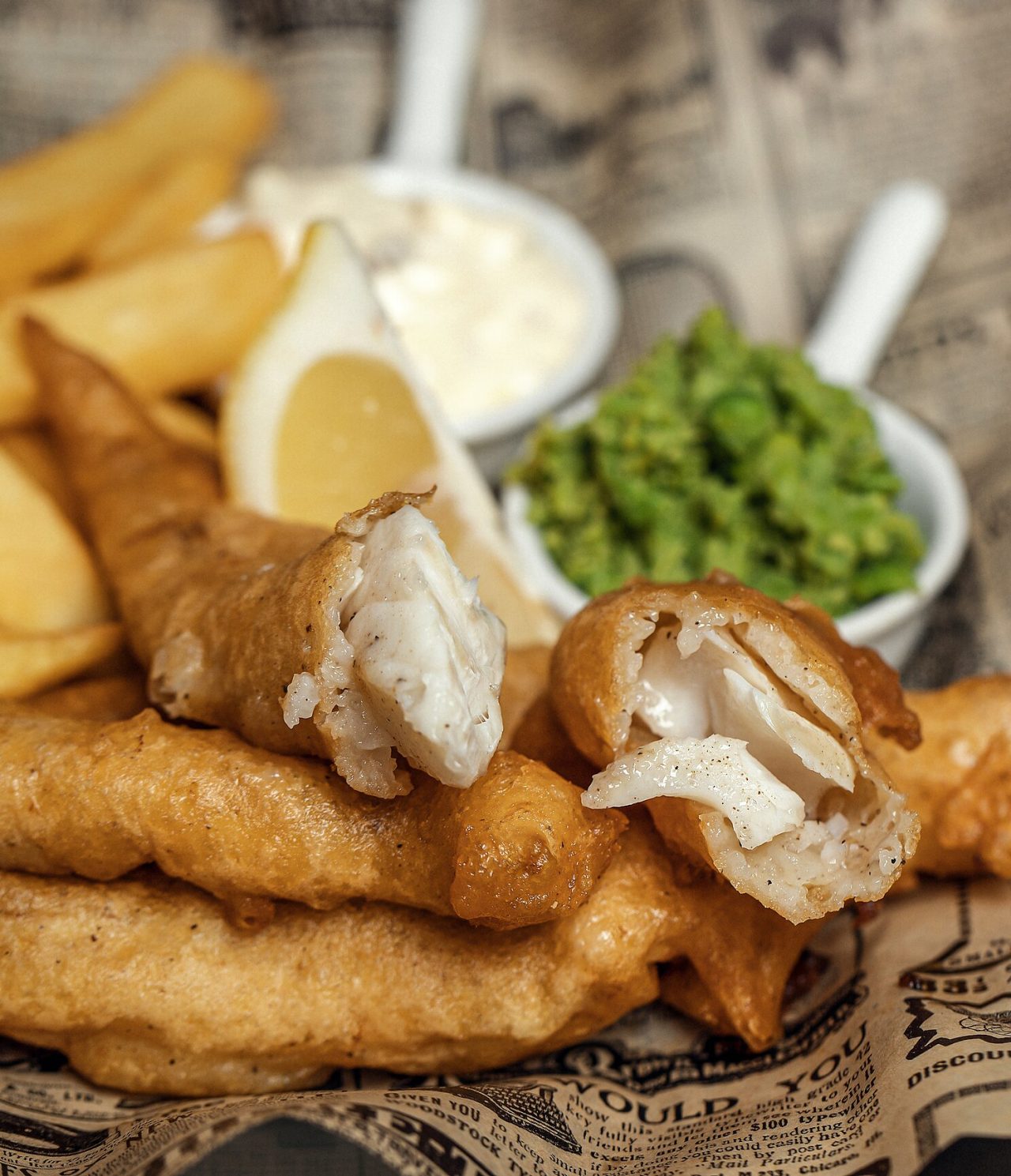 Peixe frito com batatas fritas, limão, um molho branco e uma pasta verde a acompanhar, um prato típico de Londres