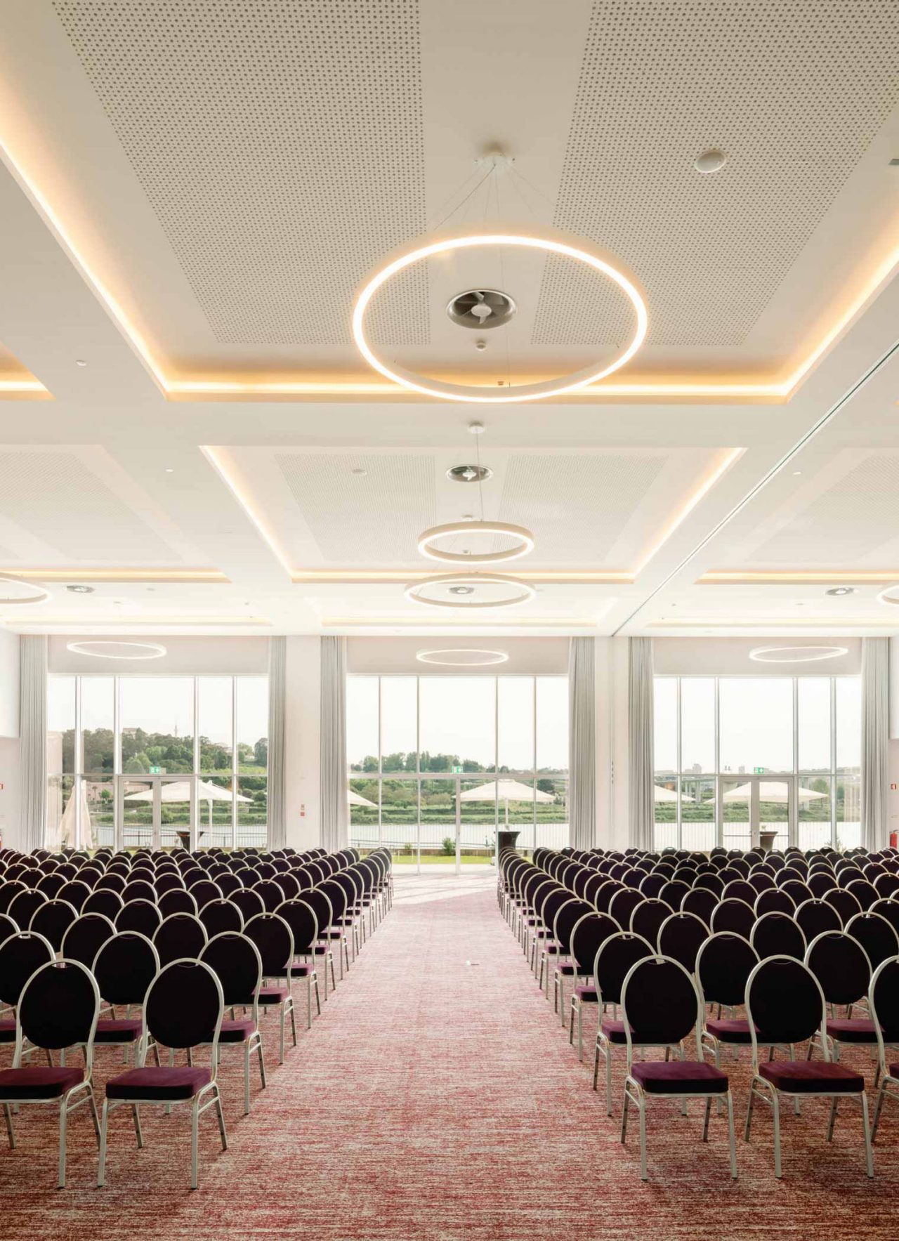 Espaço para reuniões ou conferências, em sala ampla com várias cadeiras e com janelas que permitem luz natural