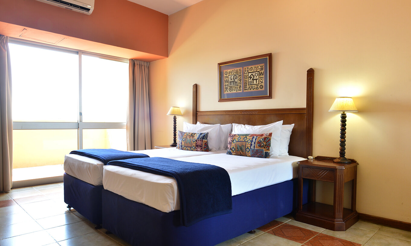The Executive Double of Pestana Rovuma has two single beds, two nightstands, and a large window with balcony