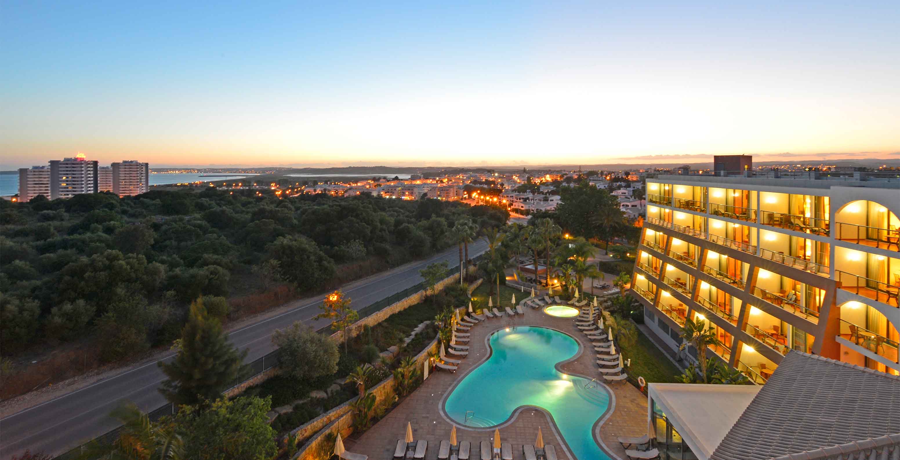 Aerial view of Pestana Alvor Park, with building, pool at sunset, Alvor in background