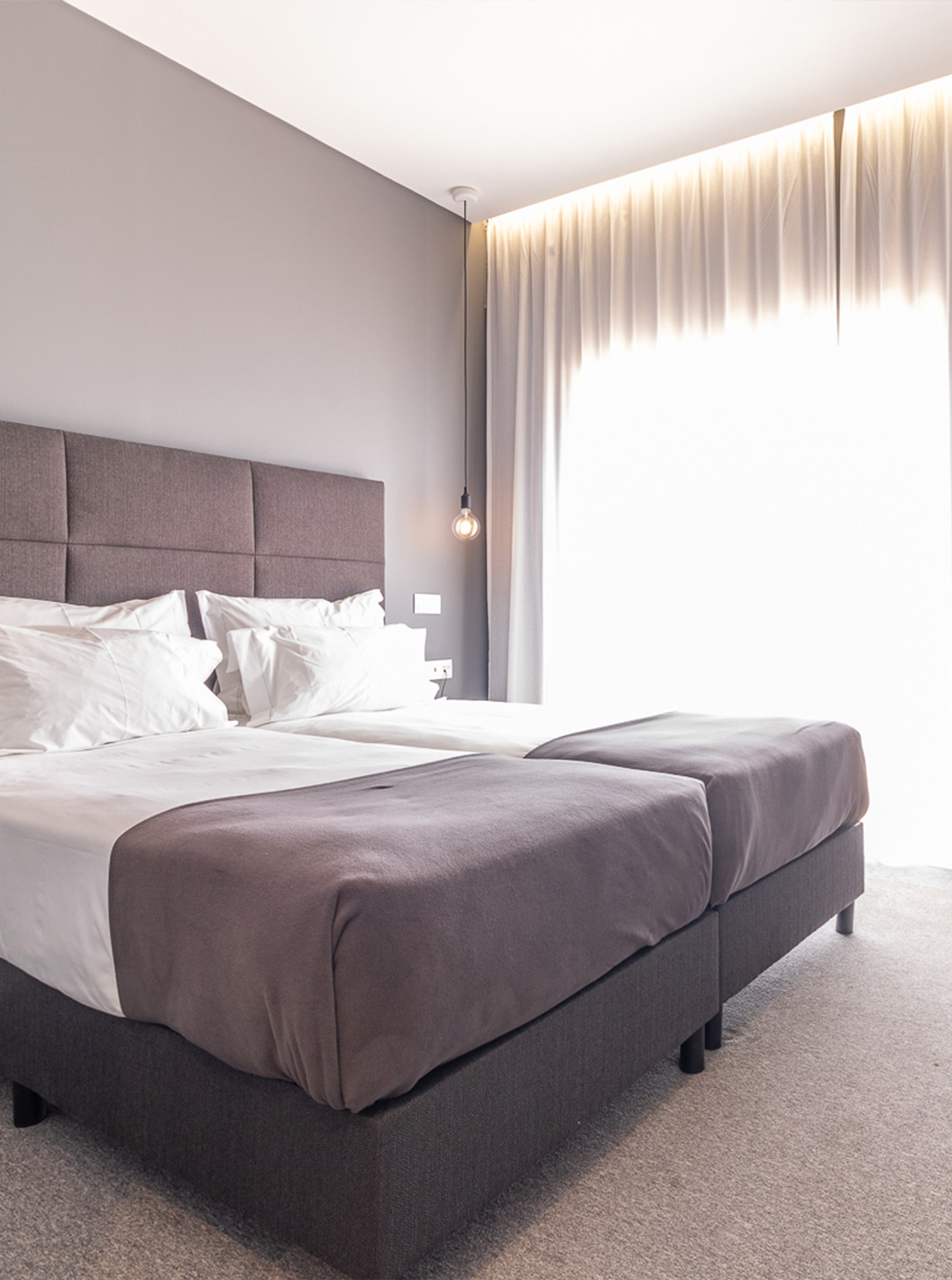 The Classic Pool View Room at Pestana Gramacho is modern with two beds, grey curtains and a table with flowers