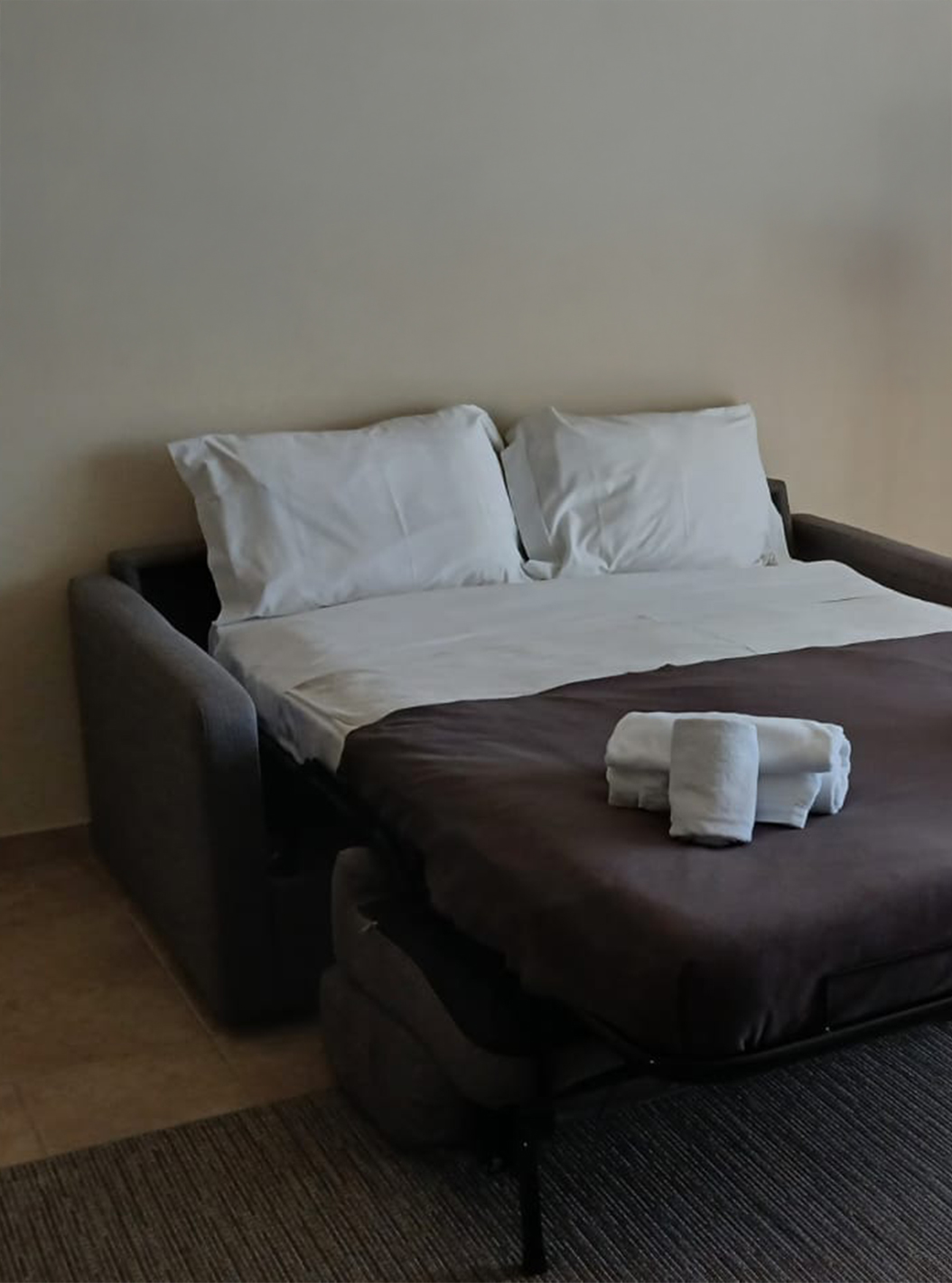 The studio at Pestana Gramacho Residences has an open sofa bed with white sheets and folded towels