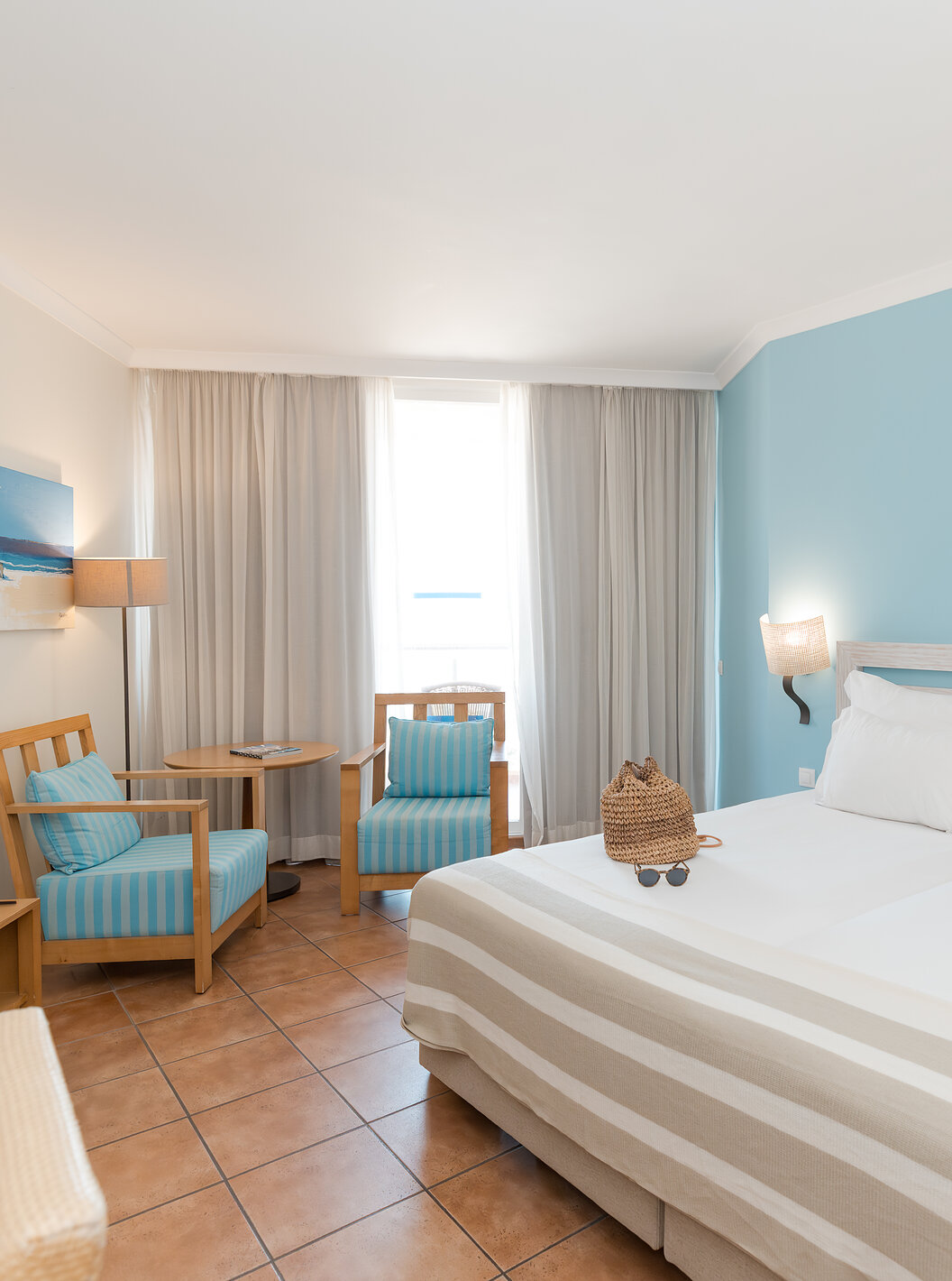 The Deluxe Side Sea View at Pestana Viking has two beds, bedside table and two armchairs by the window