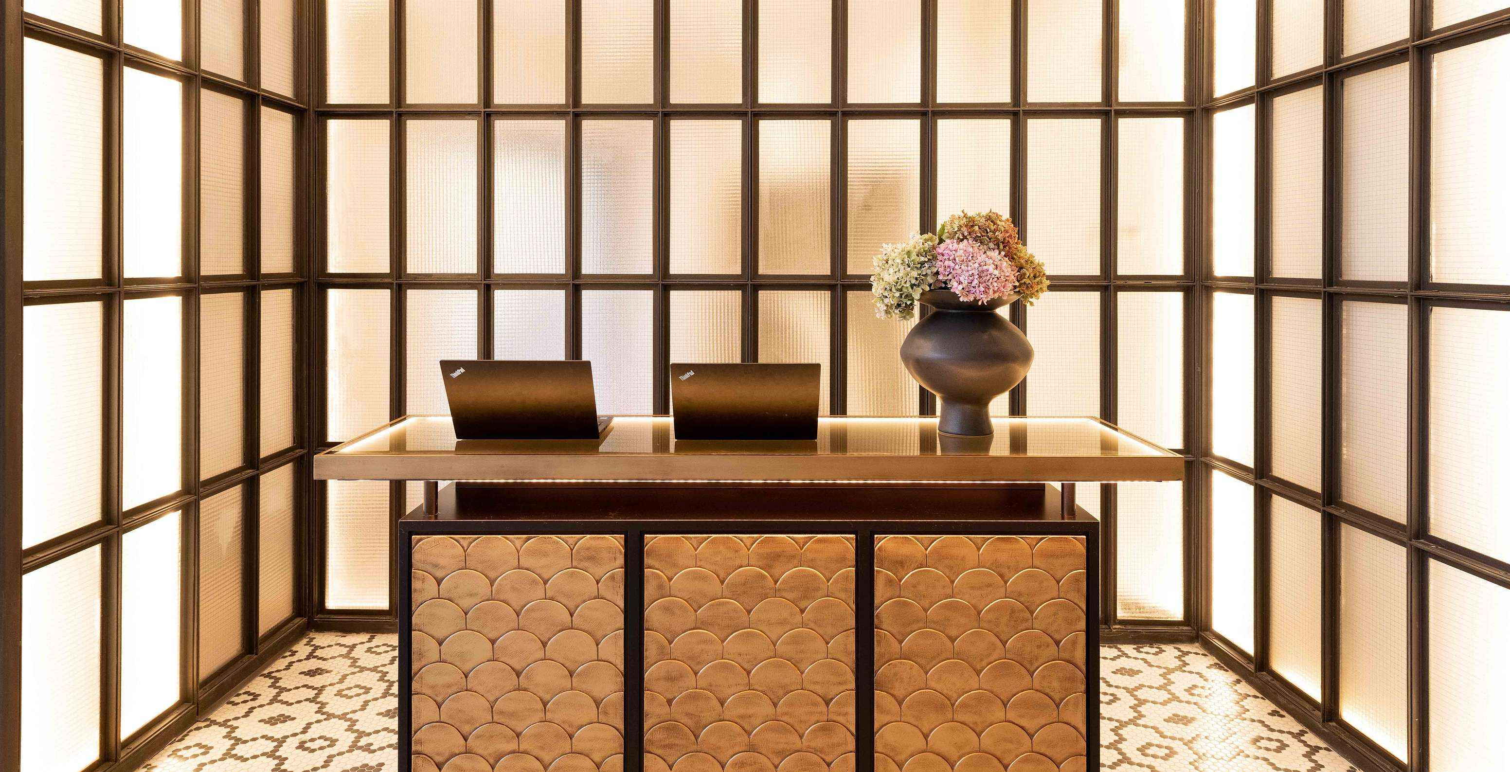 Reception desk with two laptops, a vase with flowers and a wall with illuminated rectangles