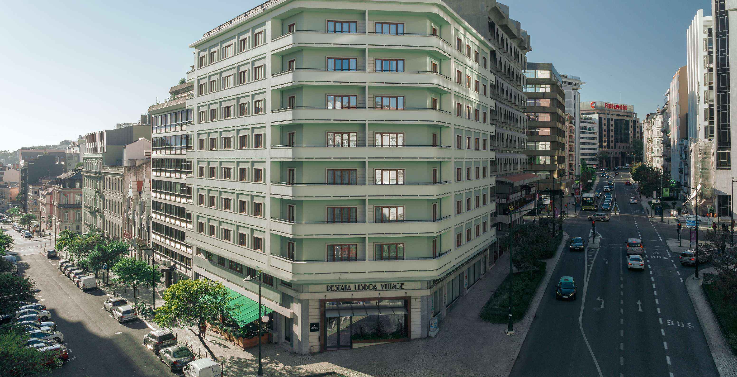 Exterior view of the green Pestana Lisboa Vintage building, with tree-lined side streets and cars on the road