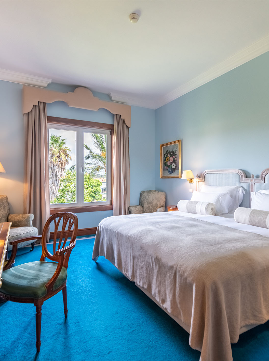 The Deluxe Garden room at Pestana Palace Lisbon has a double bed, two bedside tables, a desk, and a window with a garden view