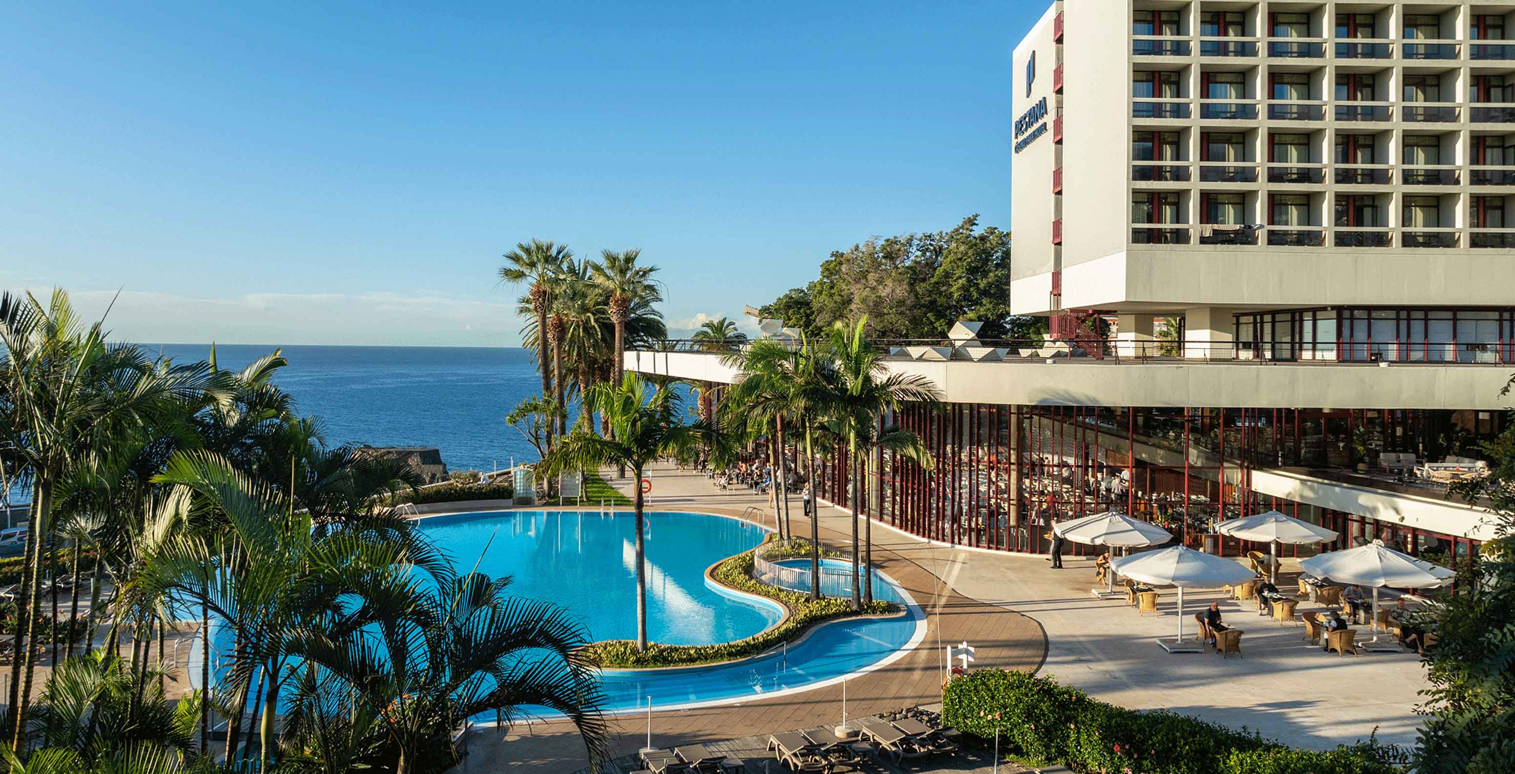 Exterior view of Pestana Casino Park, surrounded by greenery, with the city and the sea in the background 