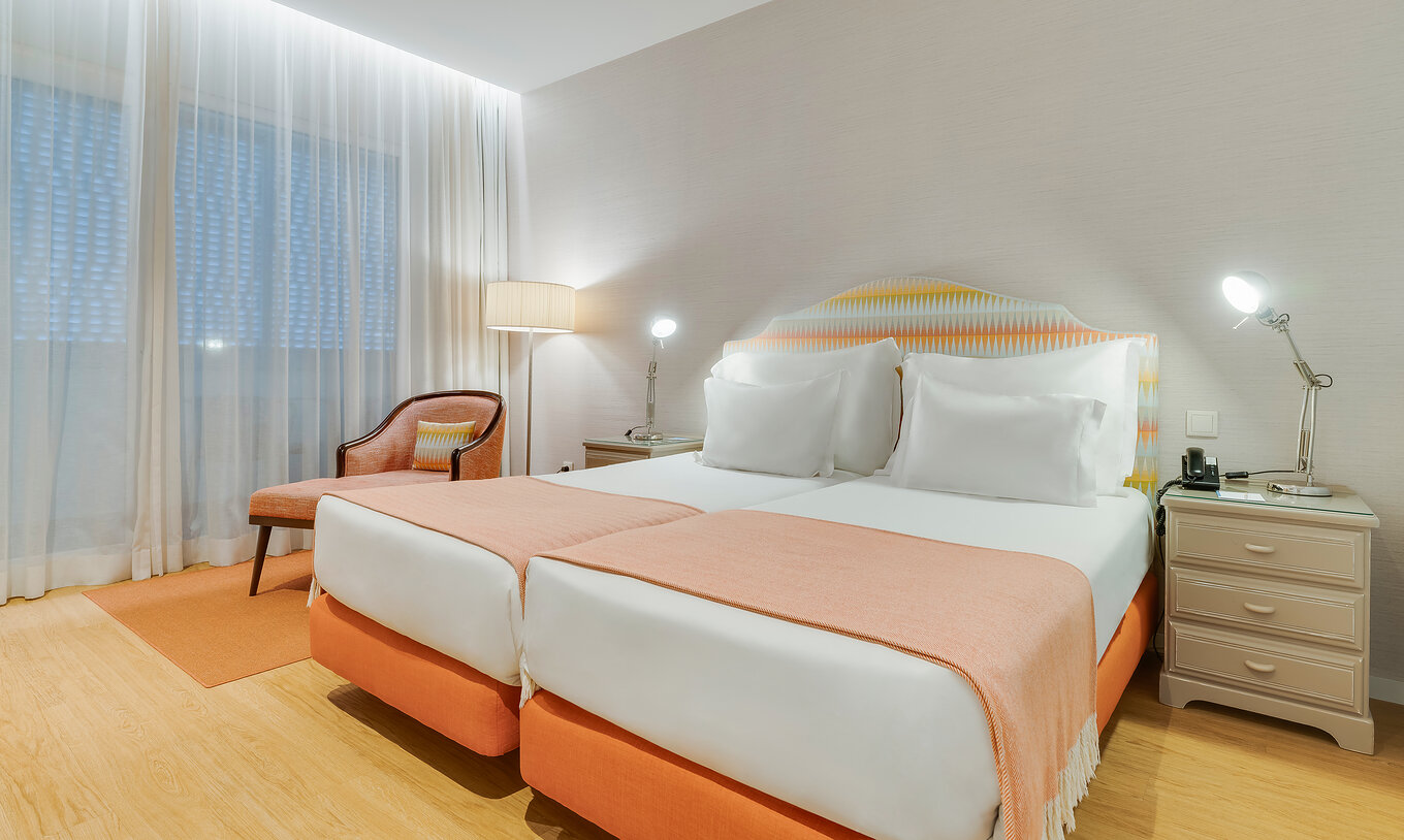 The Classic Twin Promenade View of Pestana Promenade has two beds in orange tones, an armchair, and nightstands