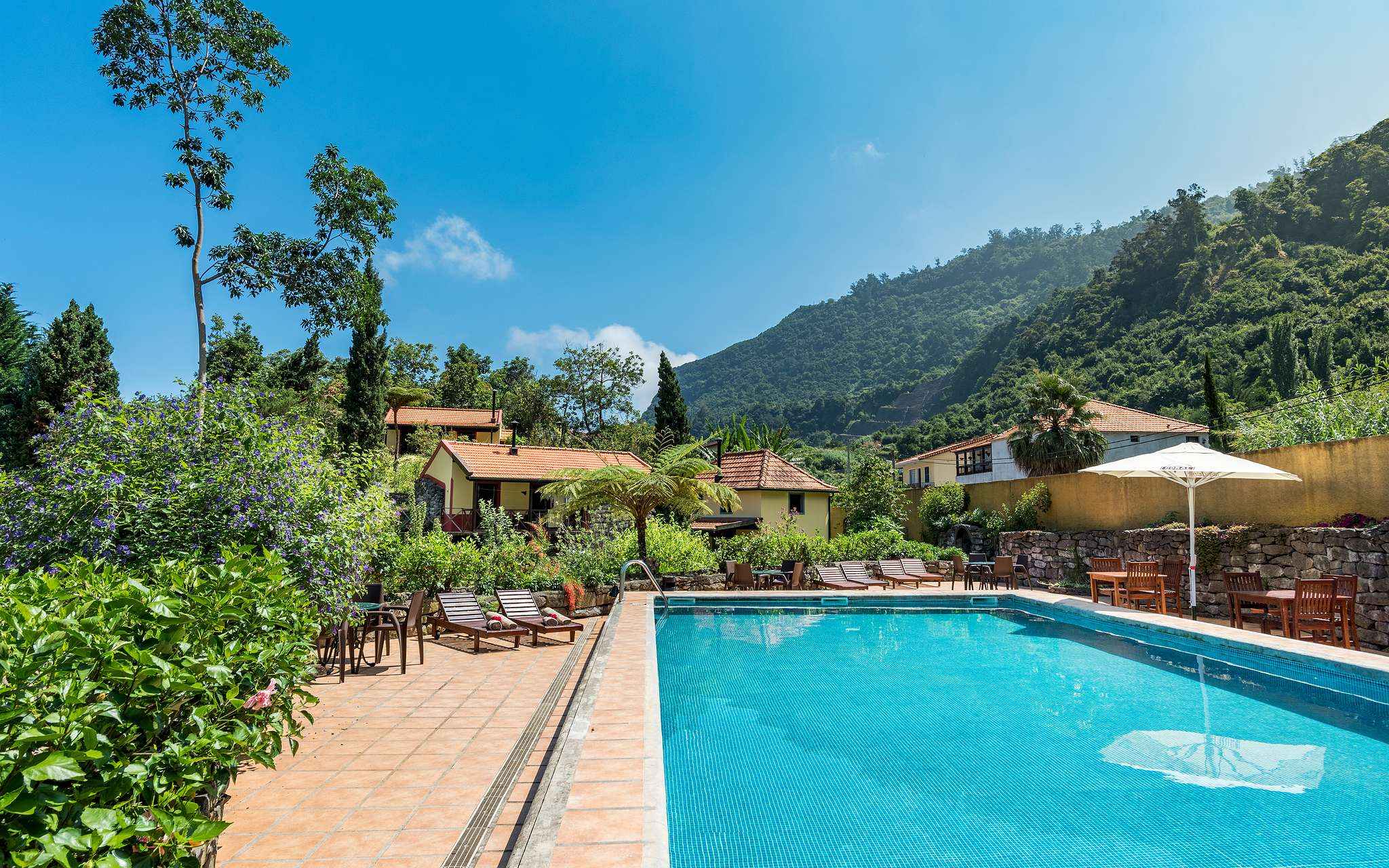 Pool of Pestana Quinta do Arco, a rural tourism hotel in Madeira, with sun loungers, vegetation, villas, and mountains