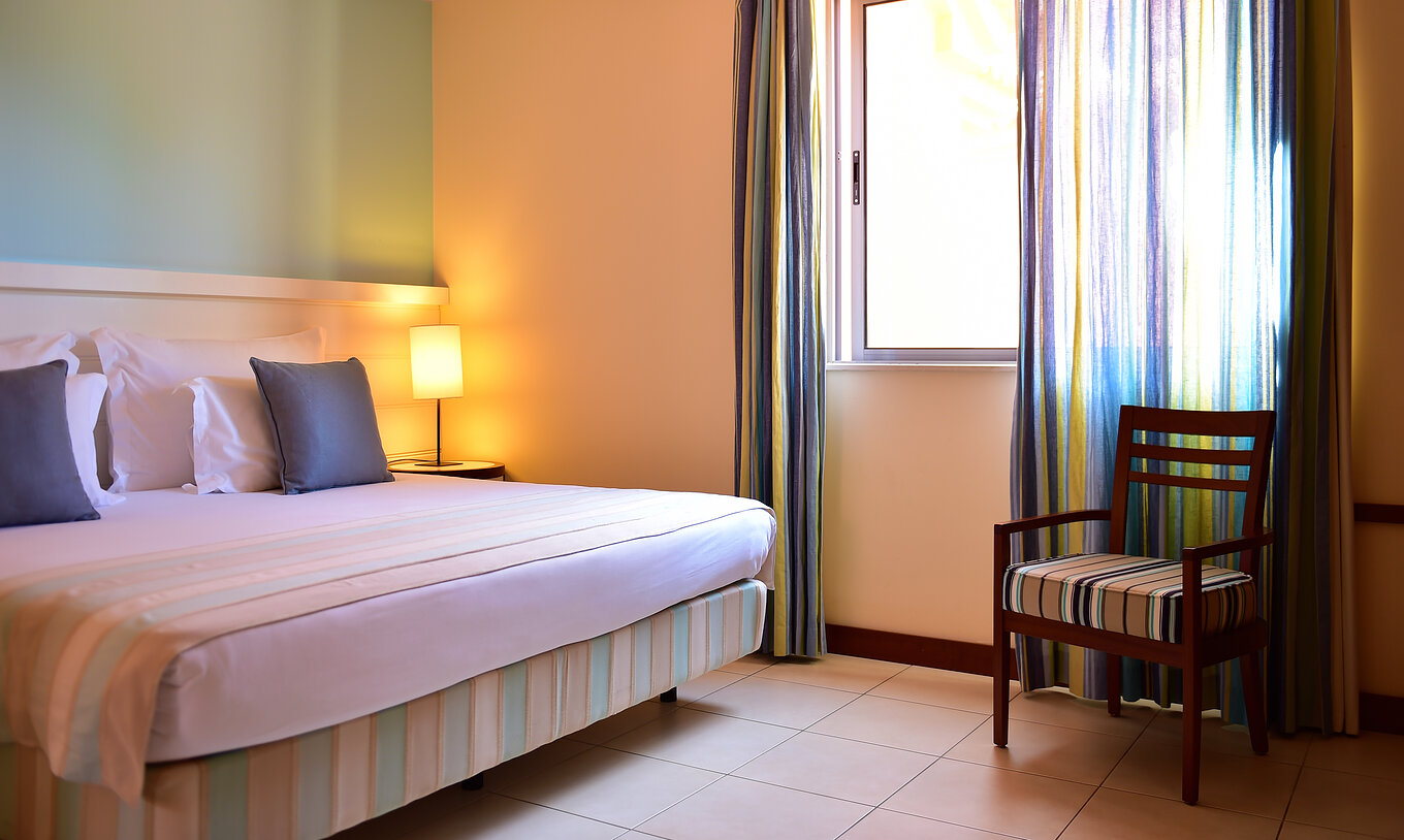The T2 Suite Apartment of Pestana Porto Santo All Inclusive has a bedroom with a double bed, a chair, and a window