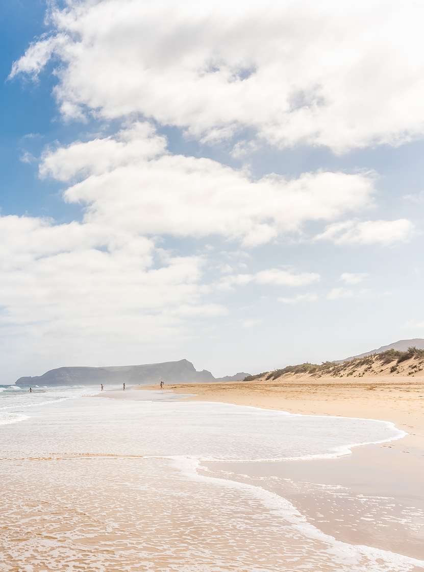 Long beach in Porto Santo with light sand, calm waves, and a blue sky with some clouds