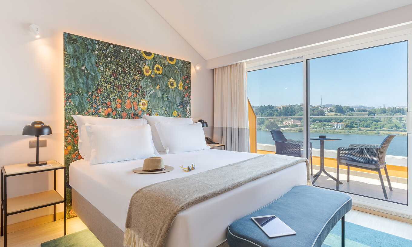 The Junior Suite at Pestana Douro Riverside includes a double bed, bedside table with a lamp, and a balcony with a view