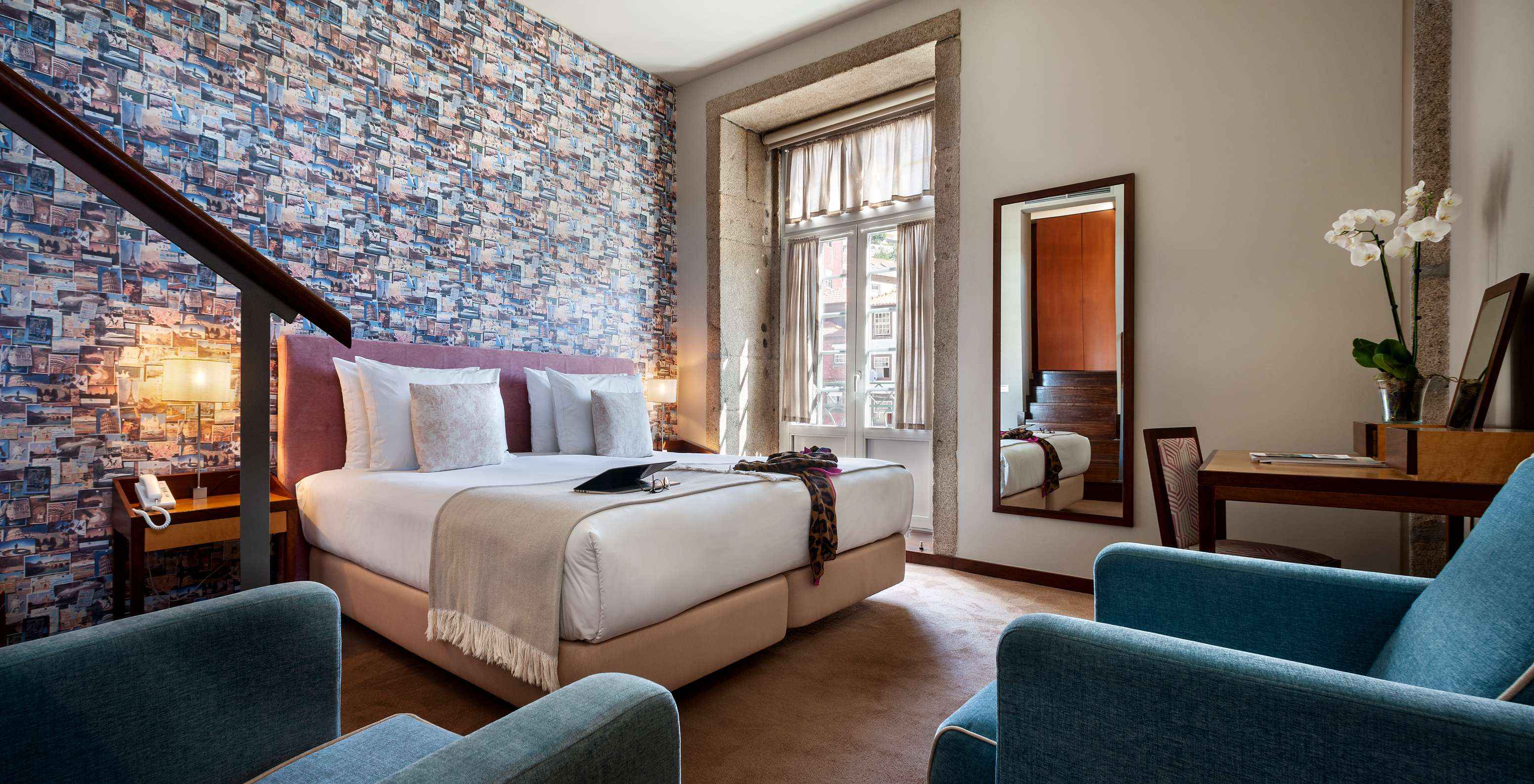 The Plaza room at Pestana Vintage Porto has a double bed, wallpaper with travel photographs, and an armchair