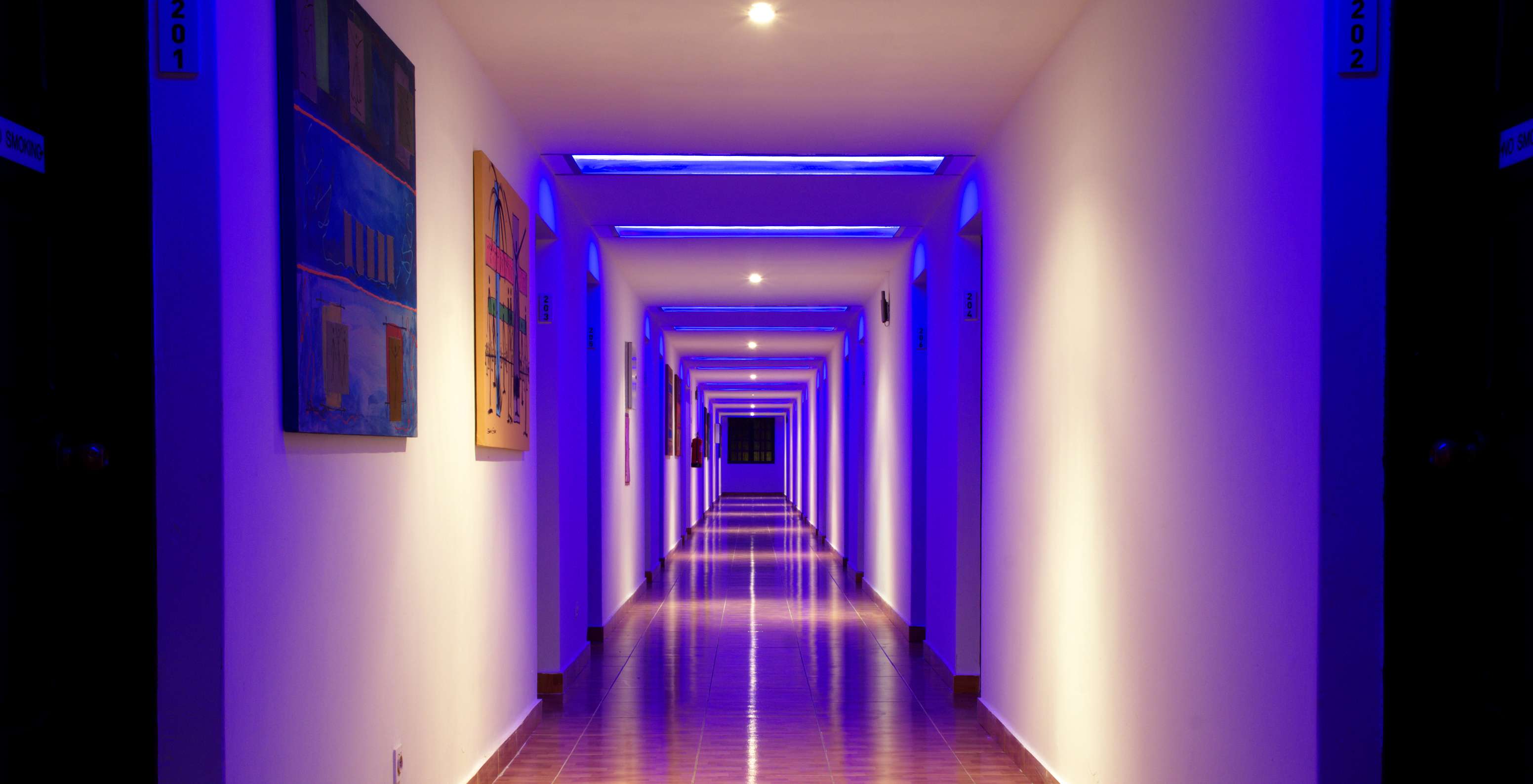 Hallway of rooms in the hotel with pool, beachfront with neon blue lights and two colorful paintings