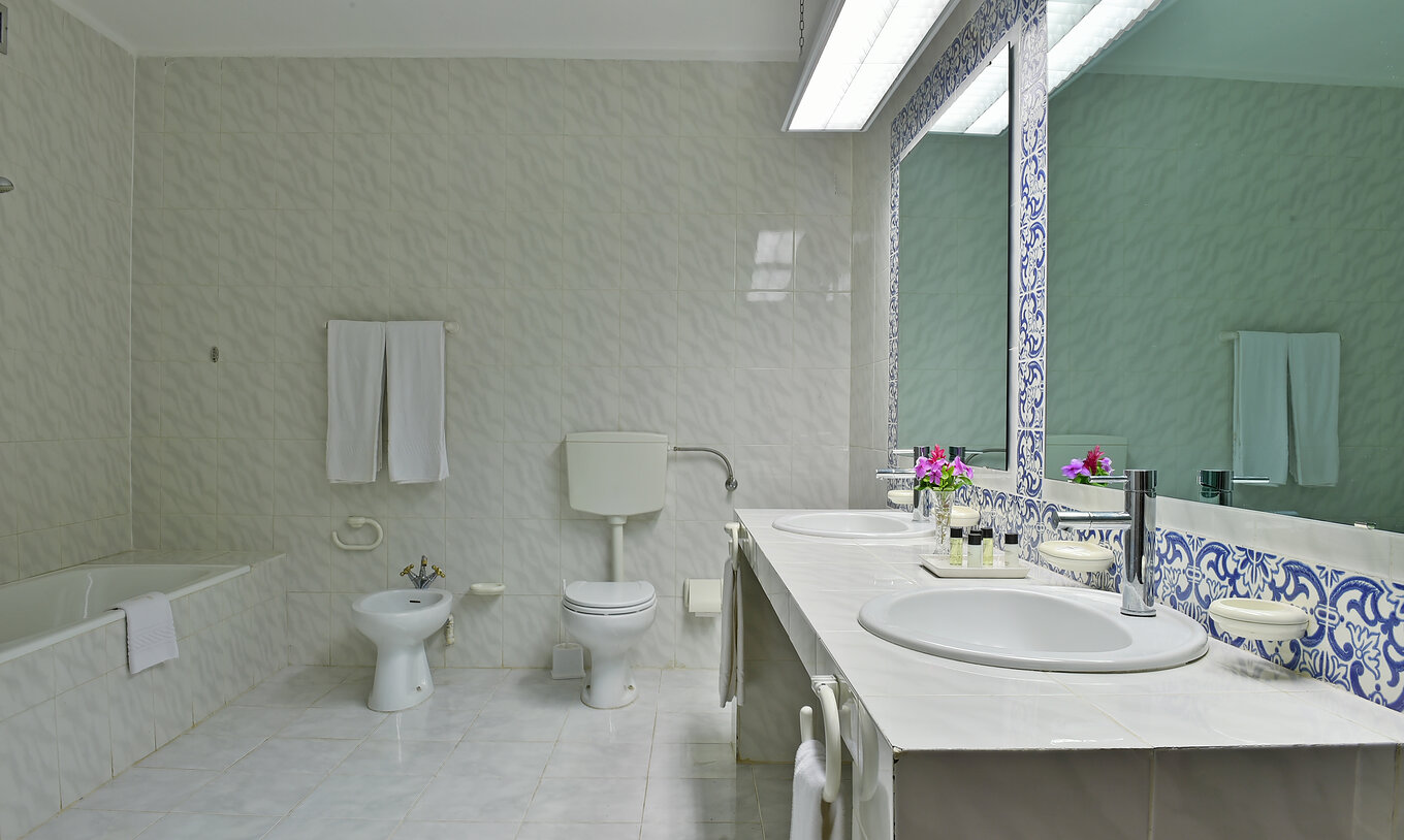 The Junior Suite at Pestana Miramar São Tomé features a bathroom with tiled walls, sinks, mirrors, a bidet, and a toilet