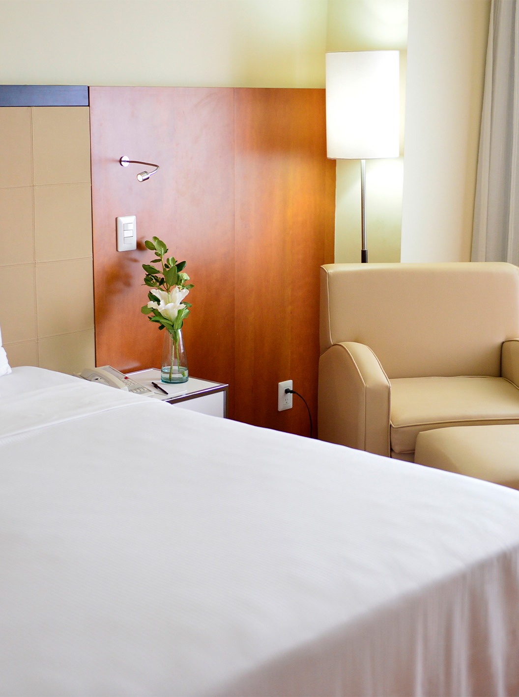 The Twin Executive Room at Pestana Caracas has a double bed, a flower on the bedside table, and a comfortable beige armchair