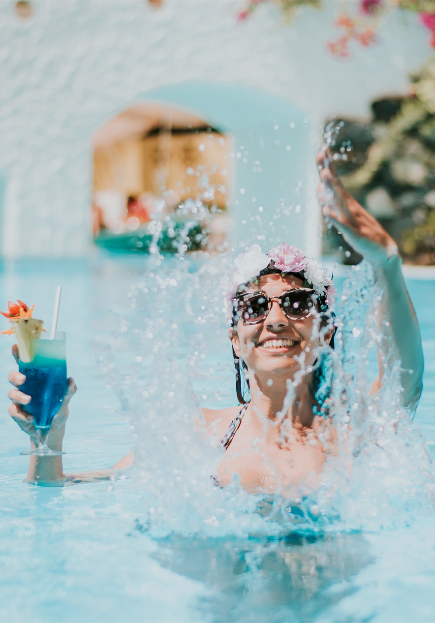 Happy woman playing with water, holding a cocktail, enjoying the all-inclusive package without worries