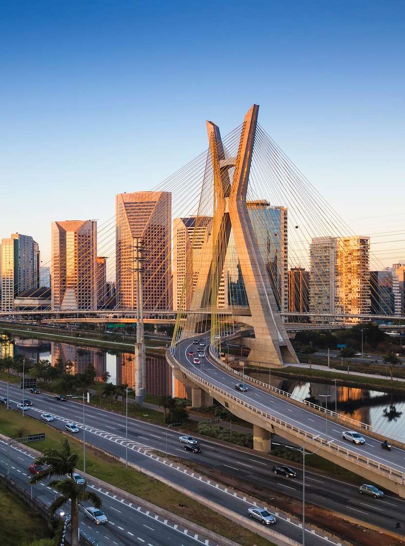Paisaje urbano de São Paulo con el Puente Estaiada cruzando el Río Pinheiros bajo un cielo azul.