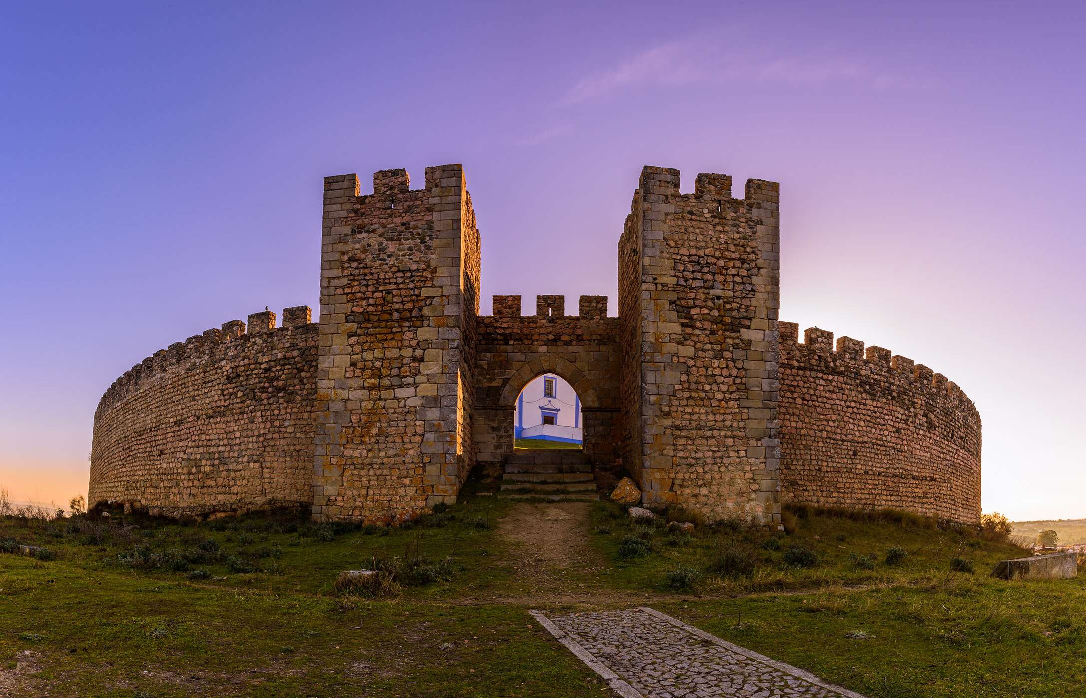 Vista frontal imponente de la entrada del castillo de Arraiolos, con muros de piedra y vegetación alrededor