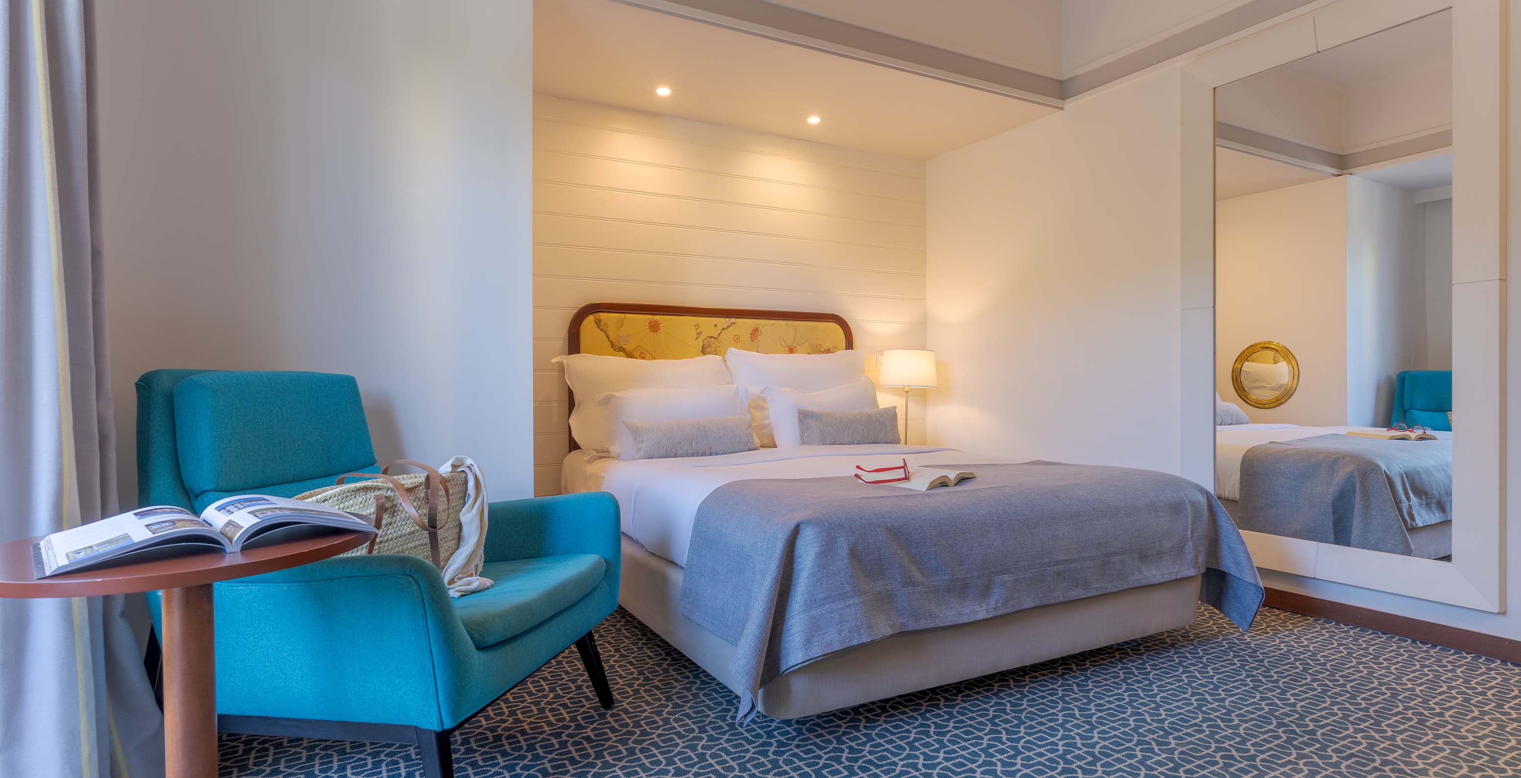 El Deluxe del Pestana Alvor Praia tiene cama matrimonial, mesa con sillón azul, espejo y alfombra geométrica