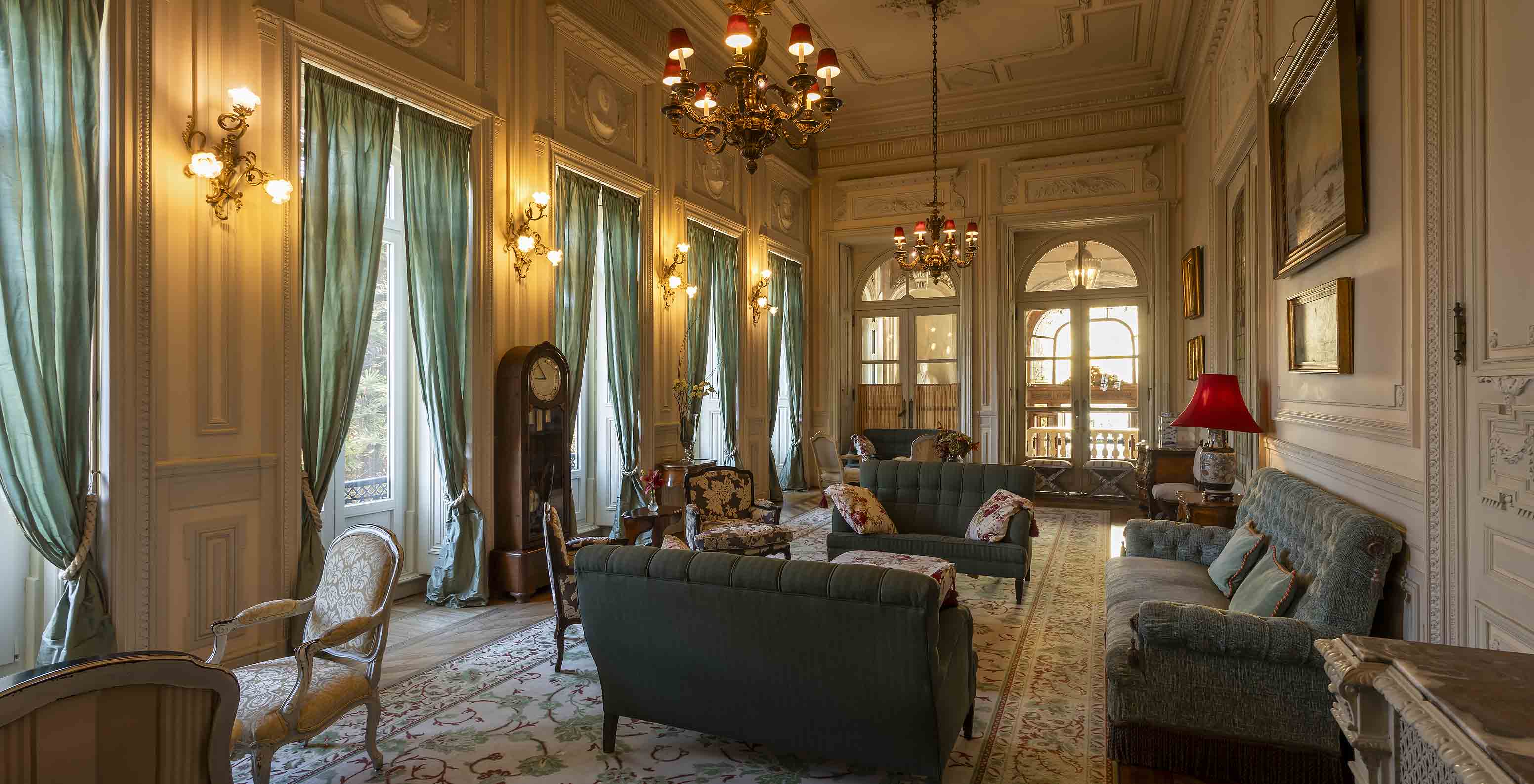 El Pestana Palace Lisboa tiene una sala de estar en el palacio con sofás, sillones y largas cortinas verdes en las ventanas