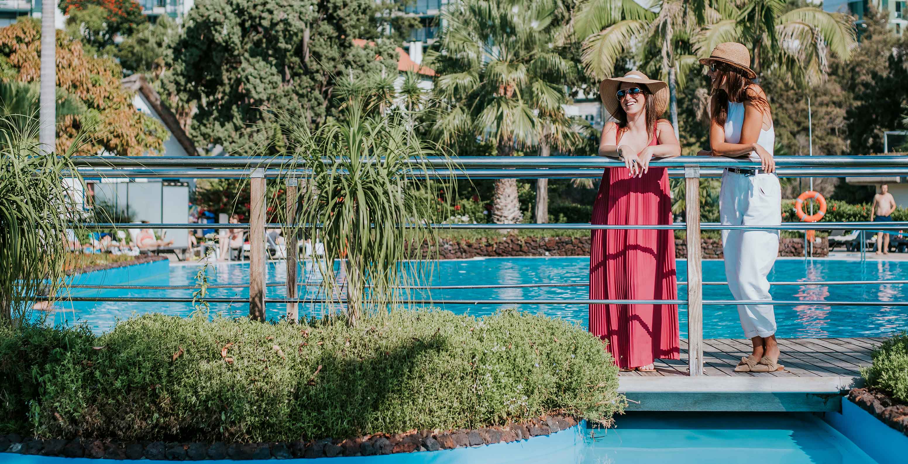 Piscina exterior del Pestana Carlton Madeira, con dos chicas sonrientes disfrutando de la vista, rodeadas de vegetación