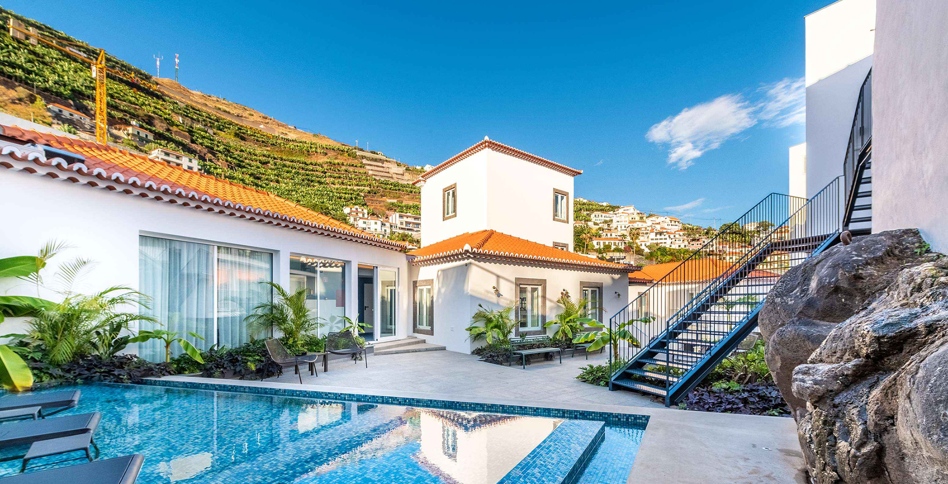 Piscina del hotel en Câmara de Lobos, en Madeira, con tumbonas dentro del agua, plantas y bancos