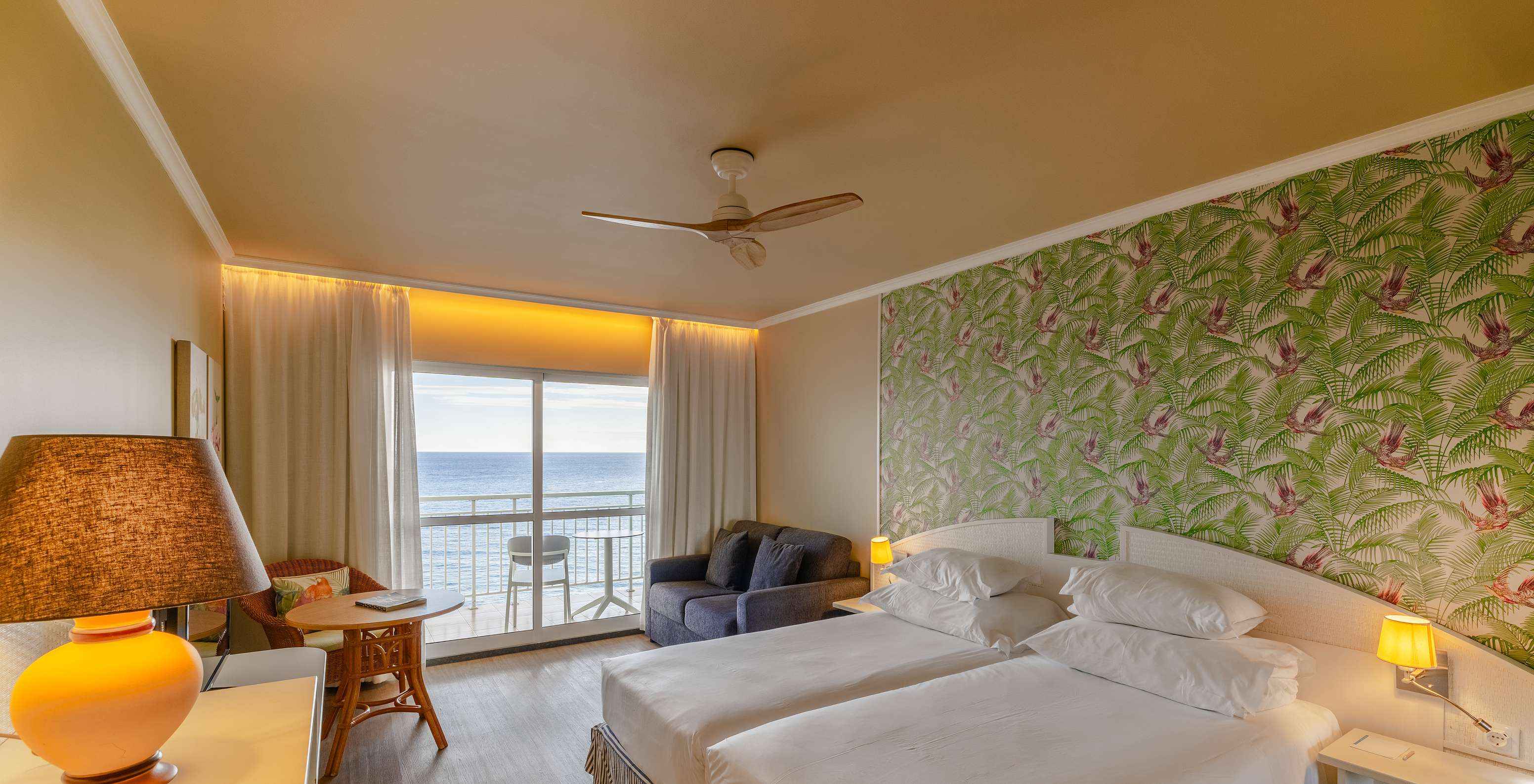 El Premium Sea View del Pestana Ocean Bay All Inclusive tiene una cama doble, papel pintado con palmeras, un sofá y balcón