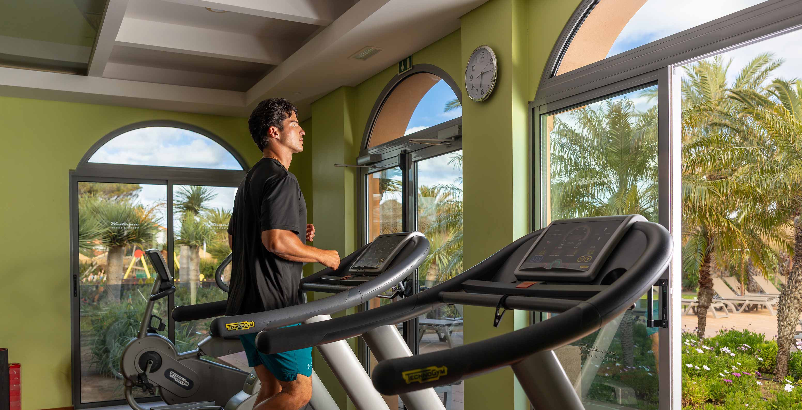 Huésped utilizando la cinta de correr en el gimnasio del Pestana Porto Santo, en una sala con vistas al jardín