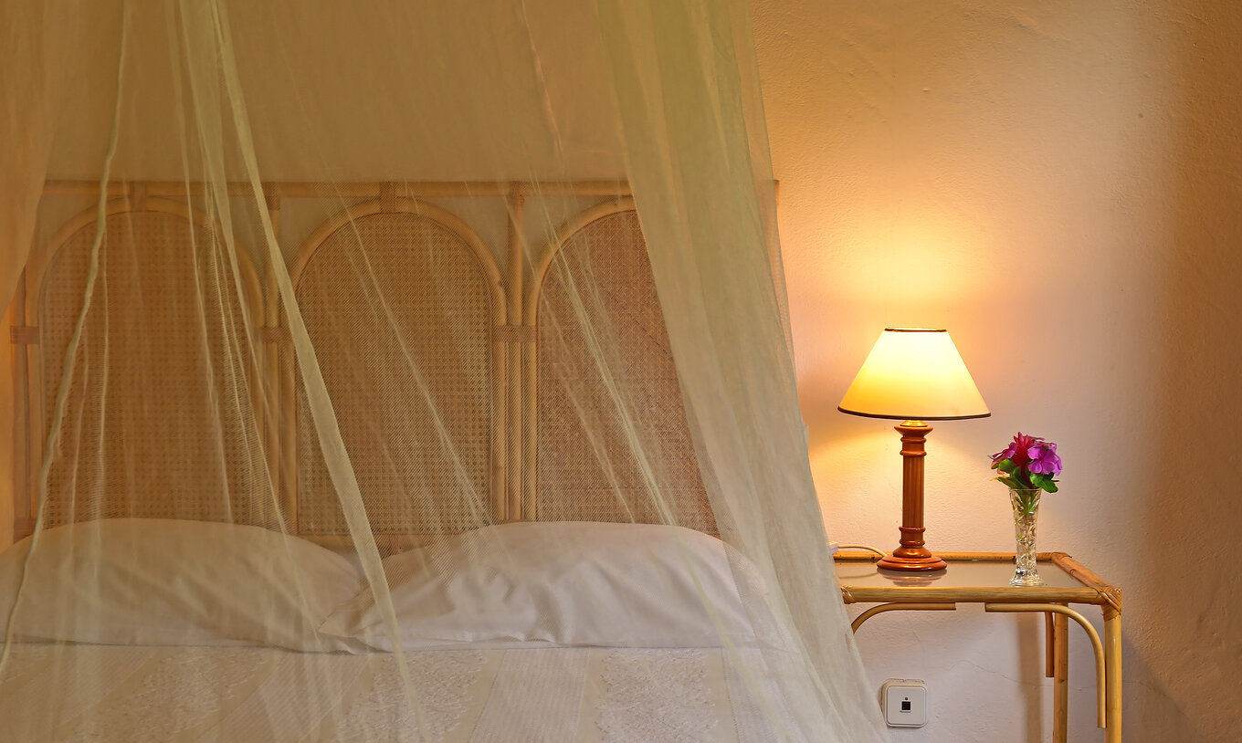 El Classic del Pestana Miramar São Tomé tiene una cama con un mosquitero y una mesa de noche con una lámpara encendida
