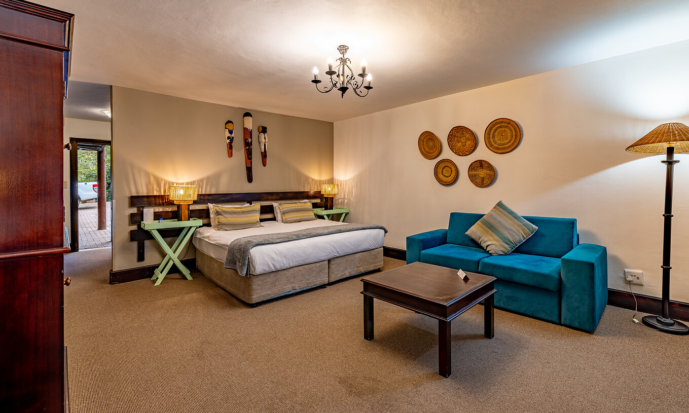 El Premium Room del Pestana Kruger Lodge tiene una cama de matrimonio, un sofá azul y decoración típica africana