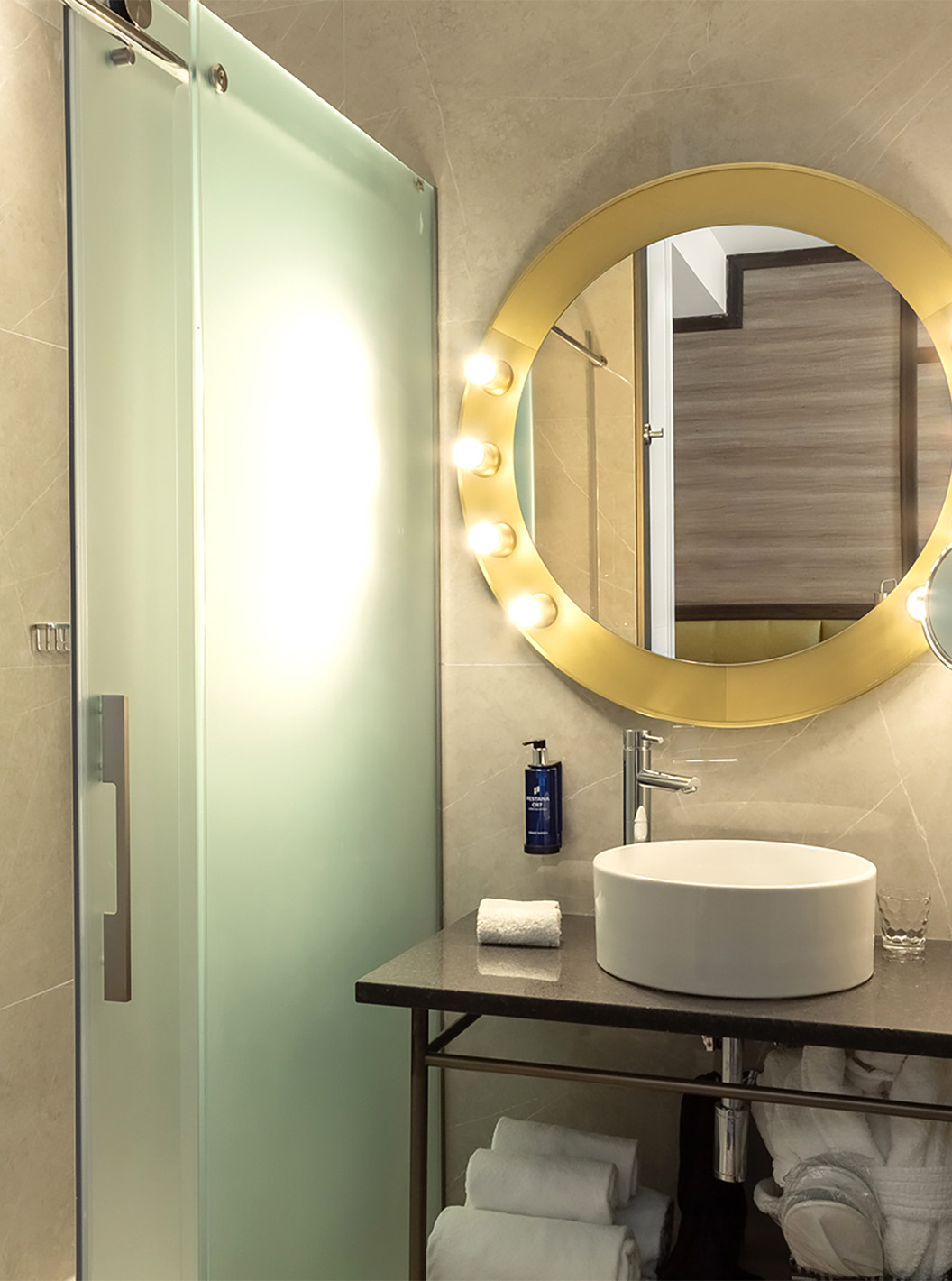 El Deluxe Grand con Vista del Pestana CR7 Gran Vía Madrid tiene un baño con un espejo, lavabo y puertas de vidrio