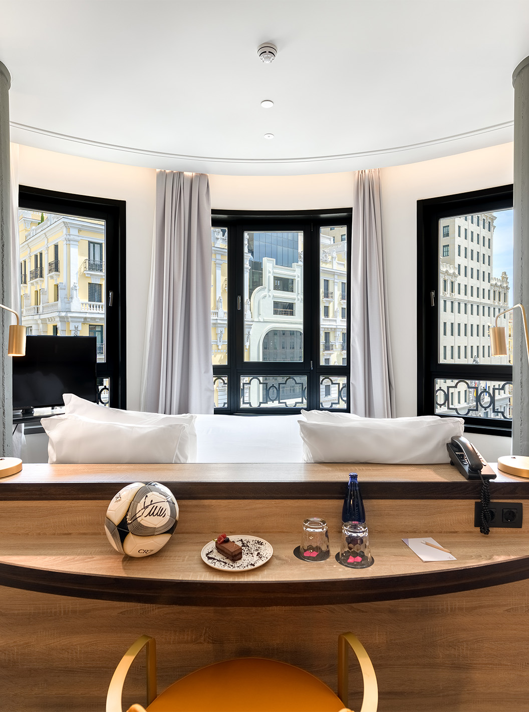 El Deluxe Grand con Vista del Pestana CR7 Gran Vía Madrid tiene una cama doble orientada hacia las ventanas en pared curva