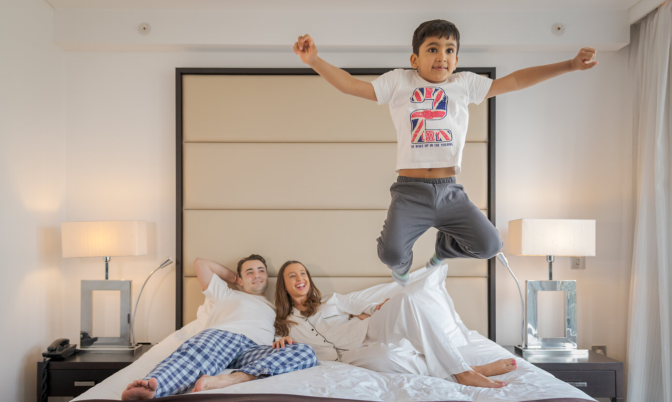 El Deluxe Family del Pestana Chelsea Bridge tiene cama doble con familia acostada y un niño saltando