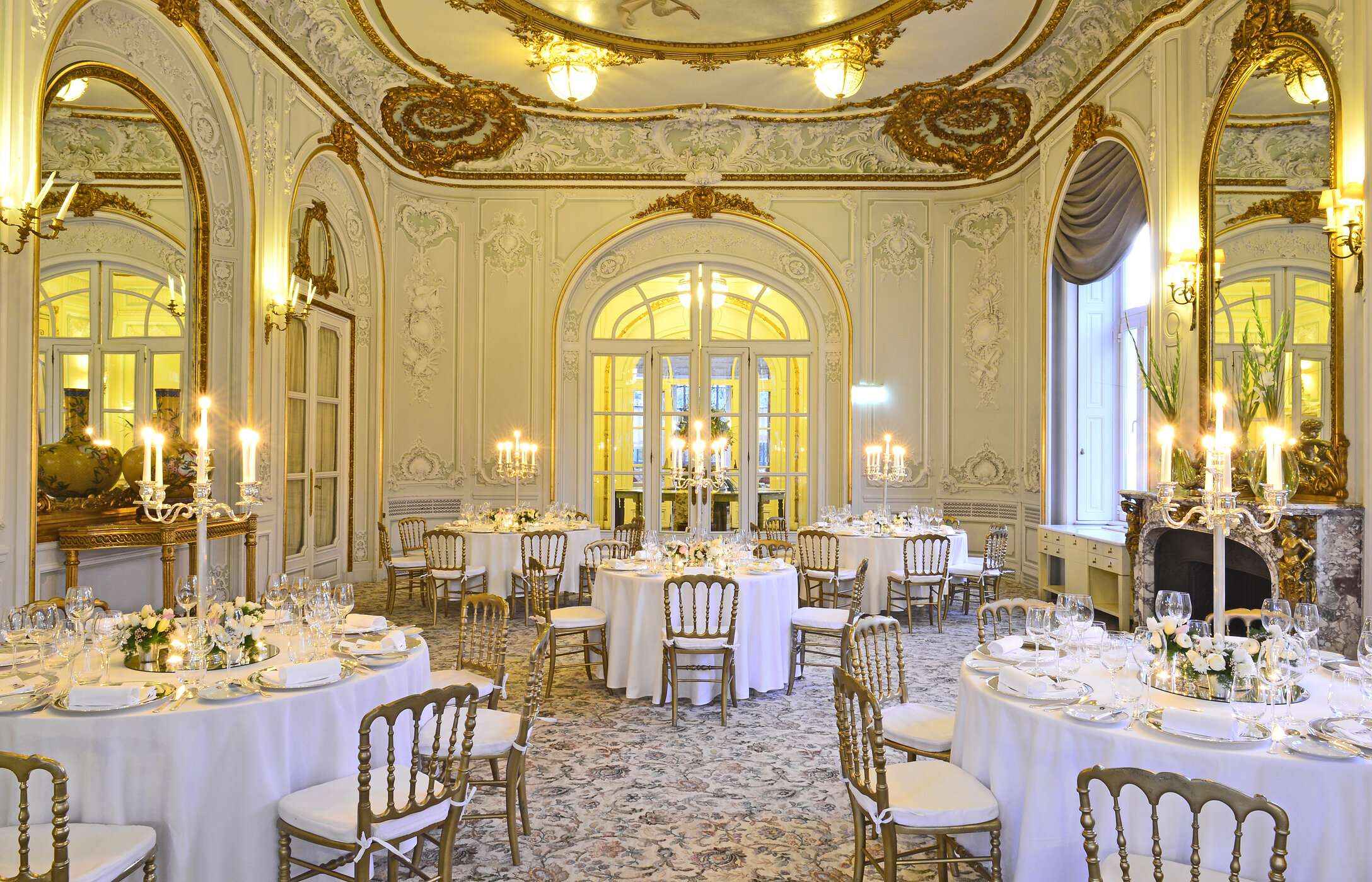 Boda en una sala elegante, con alfombra estampada, paredes adornadas con detalles dorados y mesas con arreglos florales