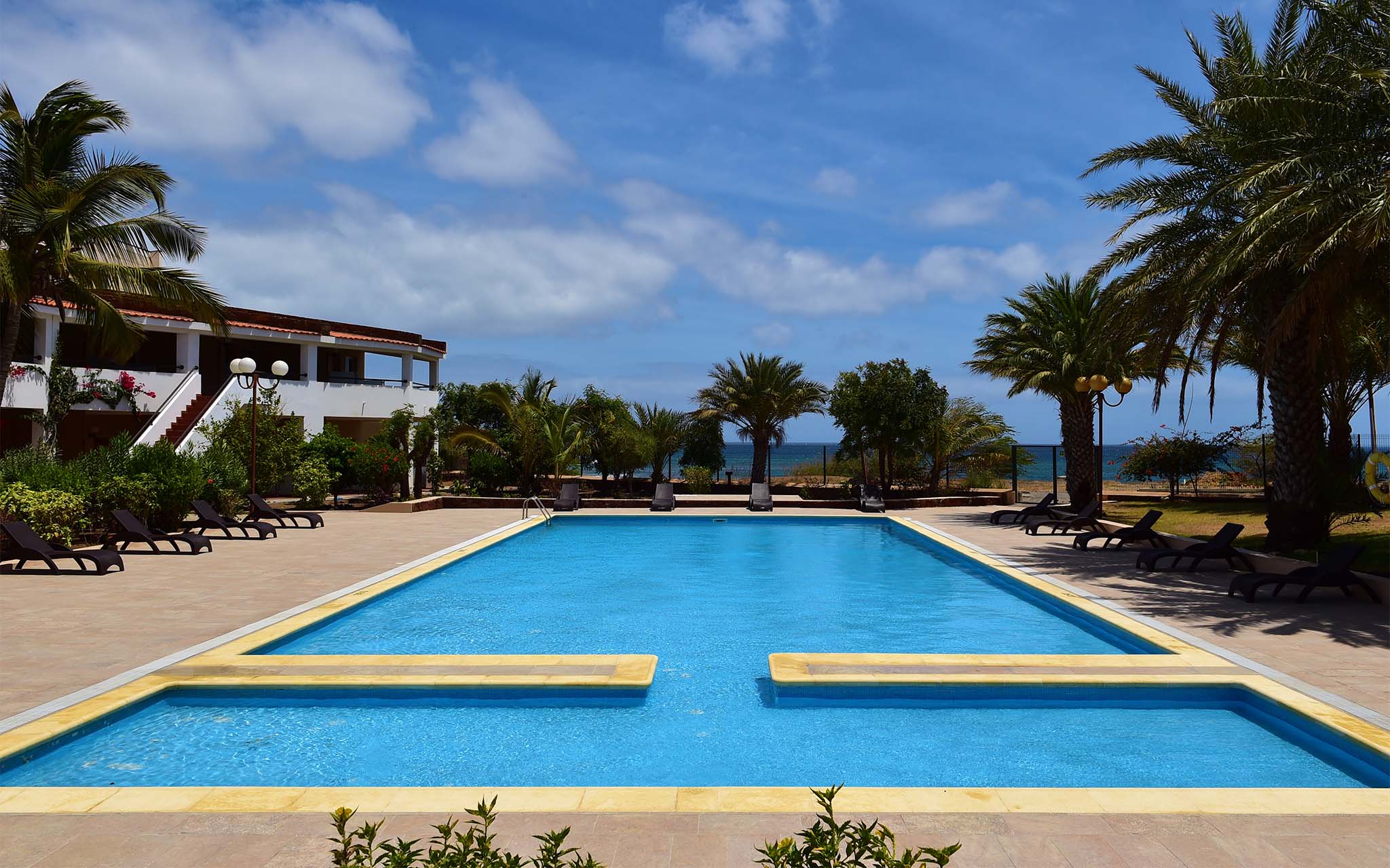 Buitenzwembad Pestana Tropico, met palmbomen en ligstoelen, en zee op achtergrond