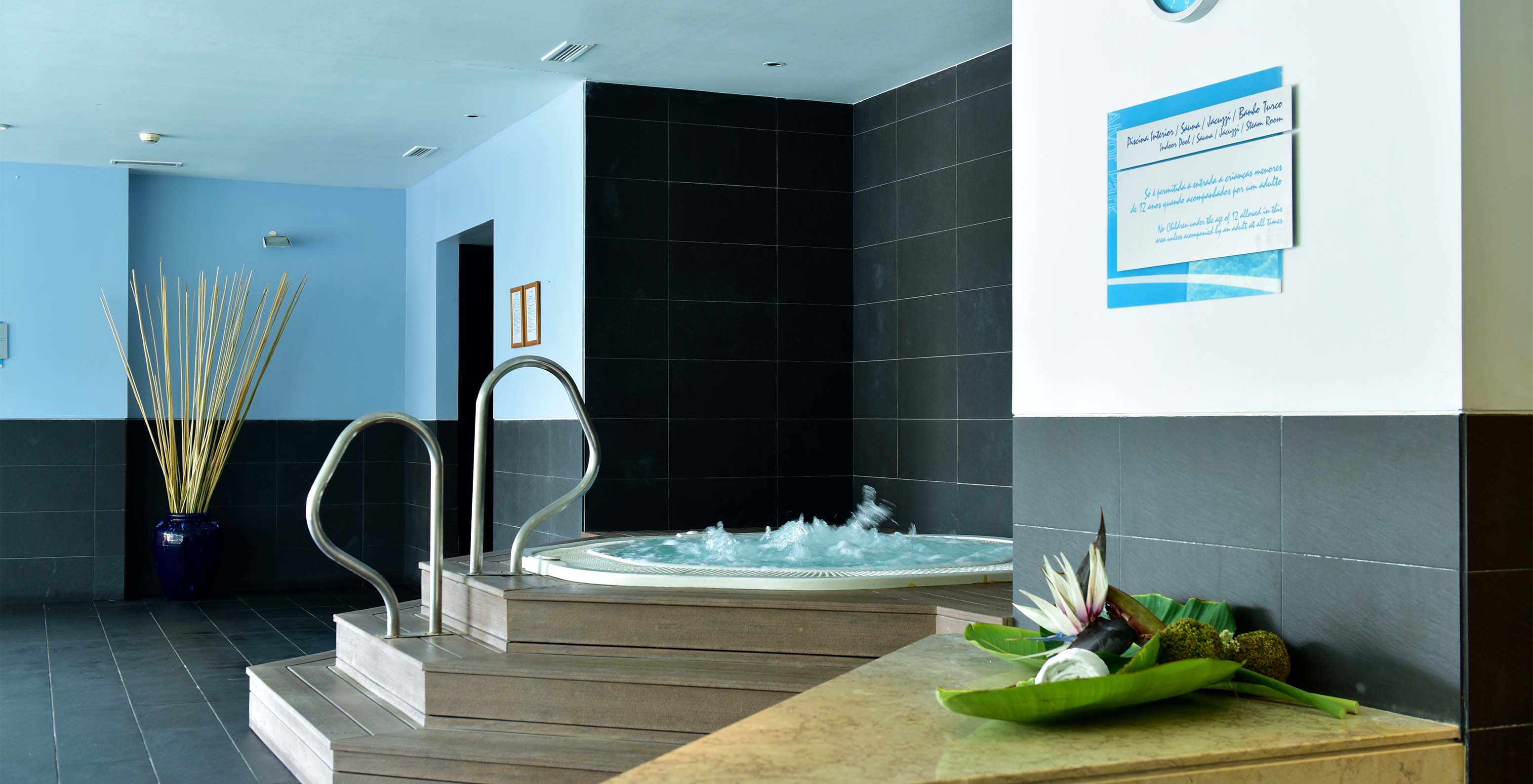 Jacuzzi met houten trappen en metalen leuningen, met zwart stenen vloer en wandklok