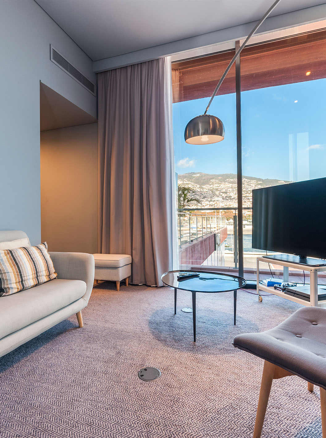 De CR7 Suite van Pestana CR7 Funchal heeft een woonkamer met bank, televisie en een raam met uitzicht op Funchal