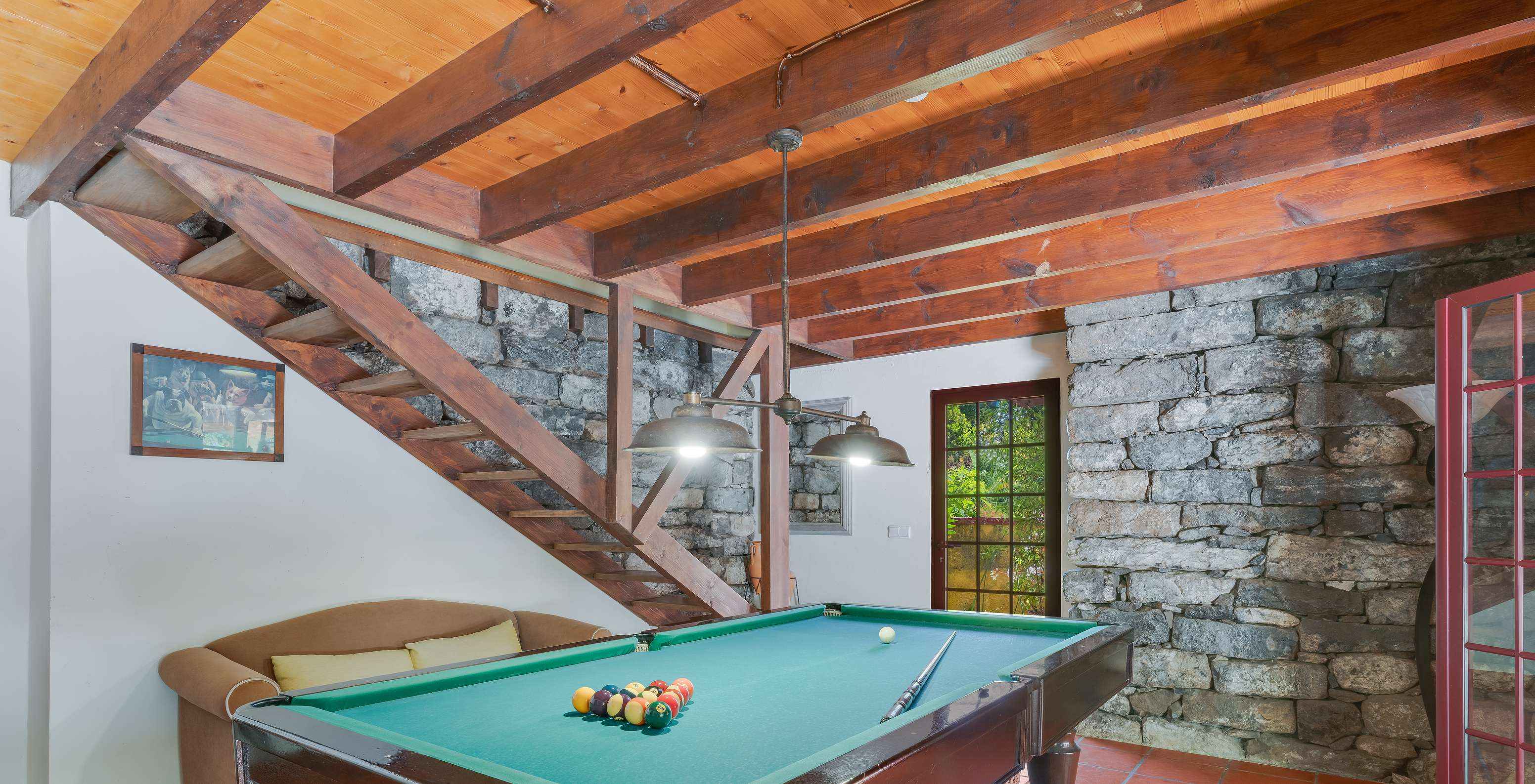 Speelkamer met biljarttafel, met bank, houten trap en stenen muren, met deuren en ramen naar buiten